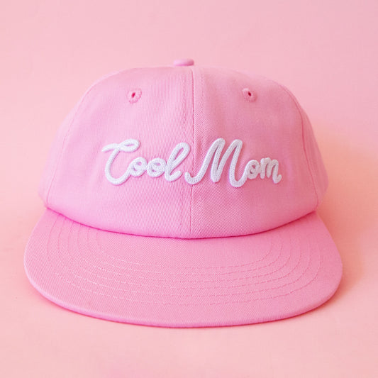 A pink flat brim hat with white embroidered text that reads, 'Cool Mom'. 