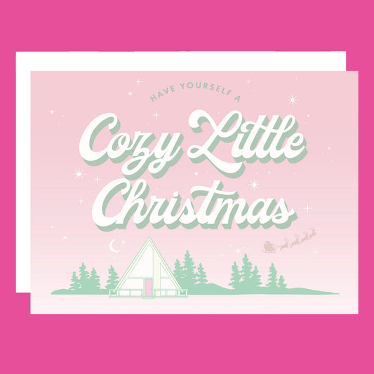 A pink and mint green Christmas card with an A-frame graphic and text above that reads, "Have Yourself A Cozy Little Christmas".