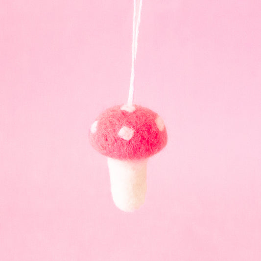 On a pink background is a felt mushroom ornament with a dark pink top and cream accents.