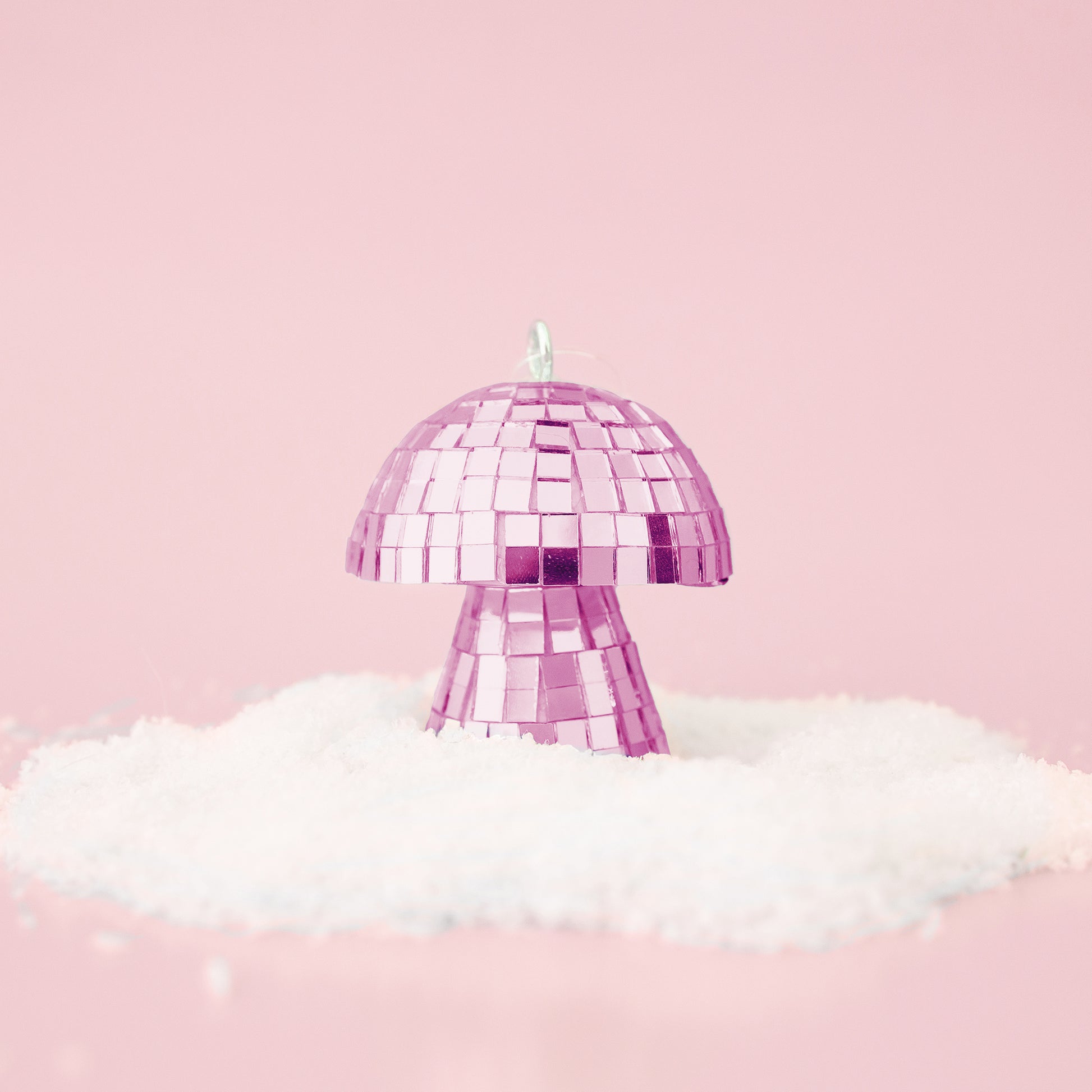 On a pink snowy background is a pink disco mushroom ornament. 