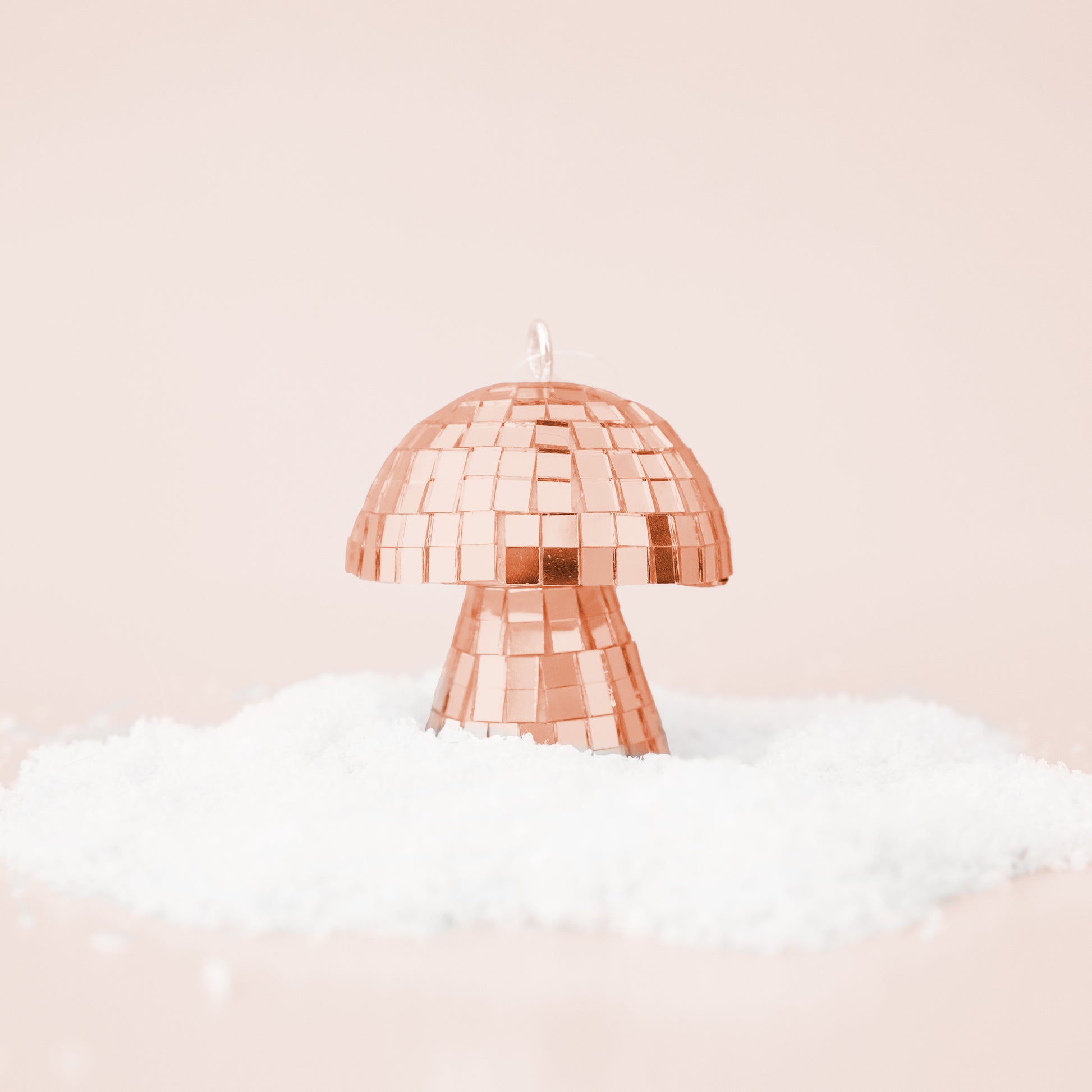 On a neutral snowy background is a rose gold disco mushroom shaped ornament. 