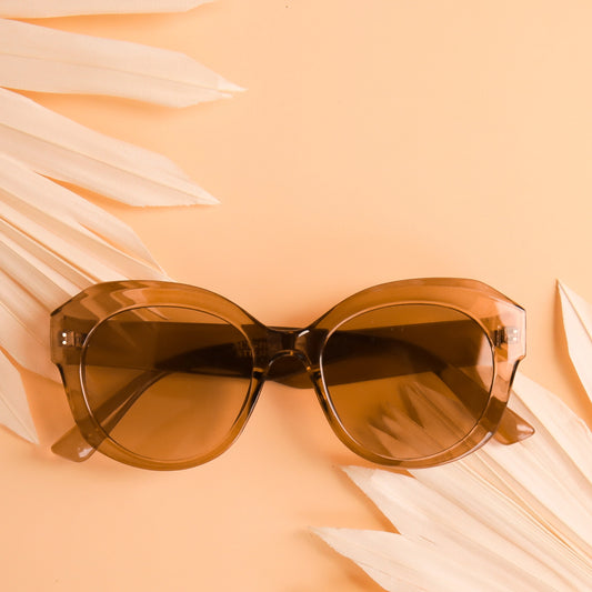 On a peachy background is a light brown translucent pair of sunglasses that have a rounded shape and a light brown lens.