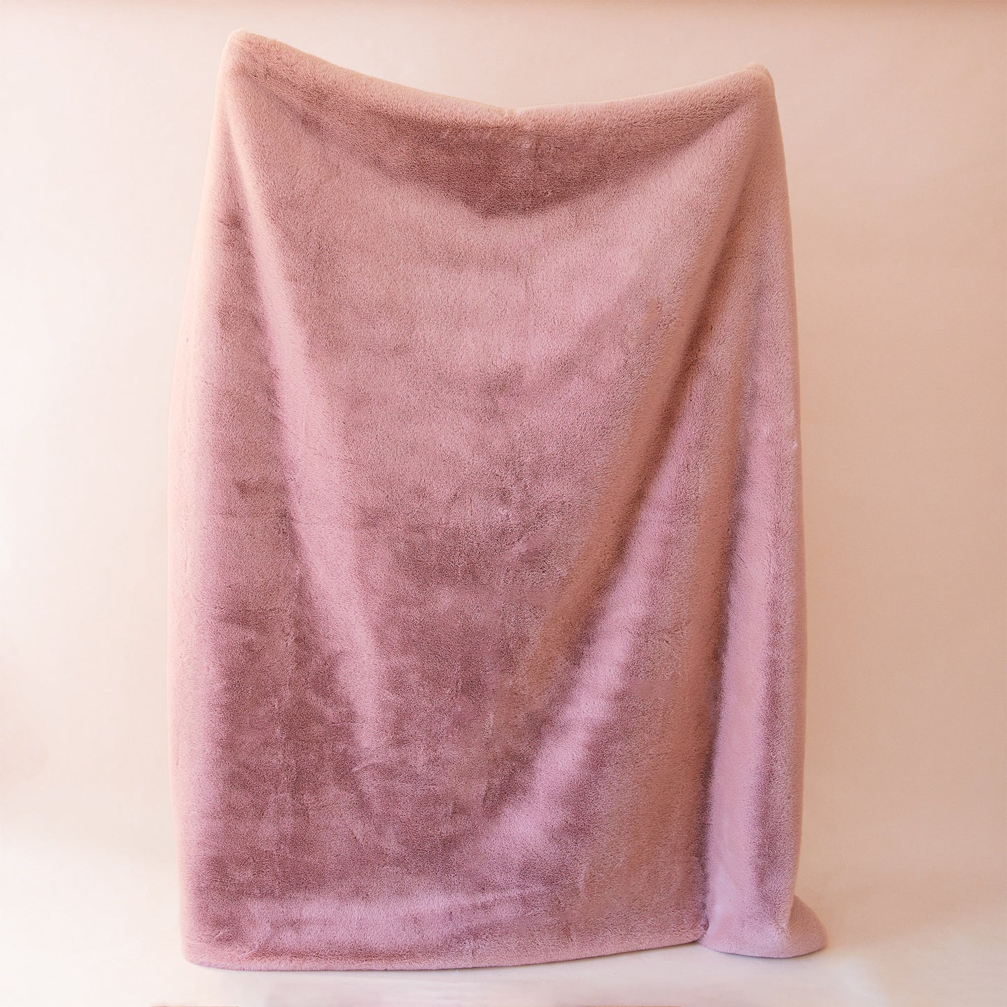 On a tan background is a dusty rose faux fur throw blanket. 