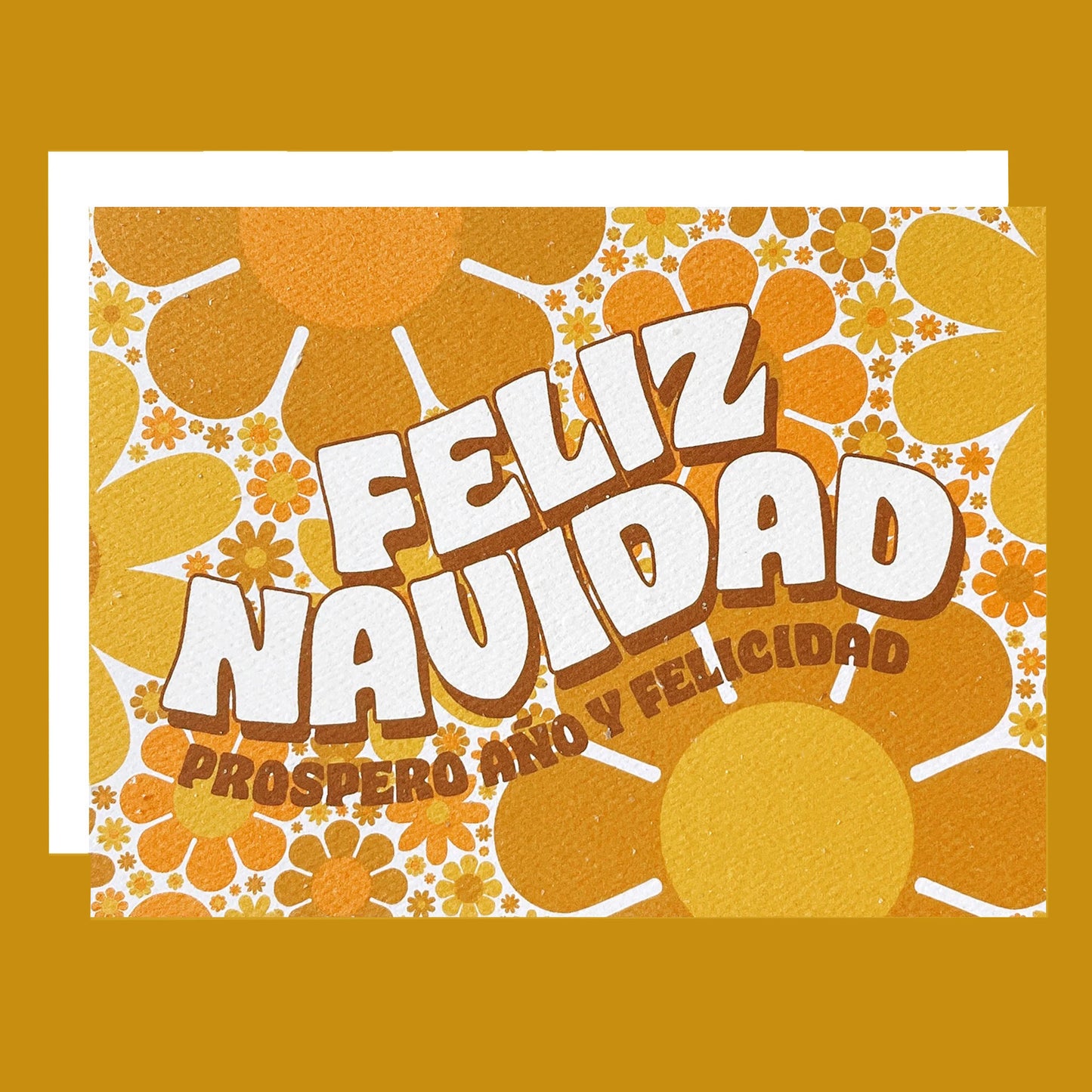 Greeting card filled with yellow and orange retro flower print. The card reads 'Feliz Navidad' in white curved bubble letters. Below reads 'prosper año y felicidad' in rust colored lettering. The card is accompanied by a solid white envelope. 