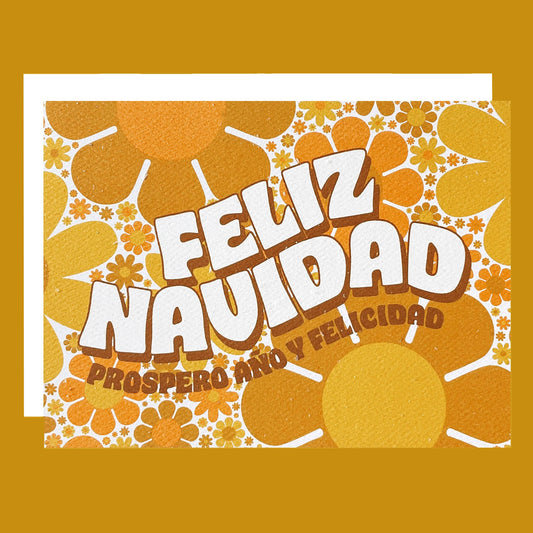 Greeting card filled with yellow and orange retro flower print. The card reads 'Feliz Navidad' in white curved bubble letters. Below reads 'prosper año y felicidad' in rust colored lettering. The card is accompanied by a solid white envelope. 