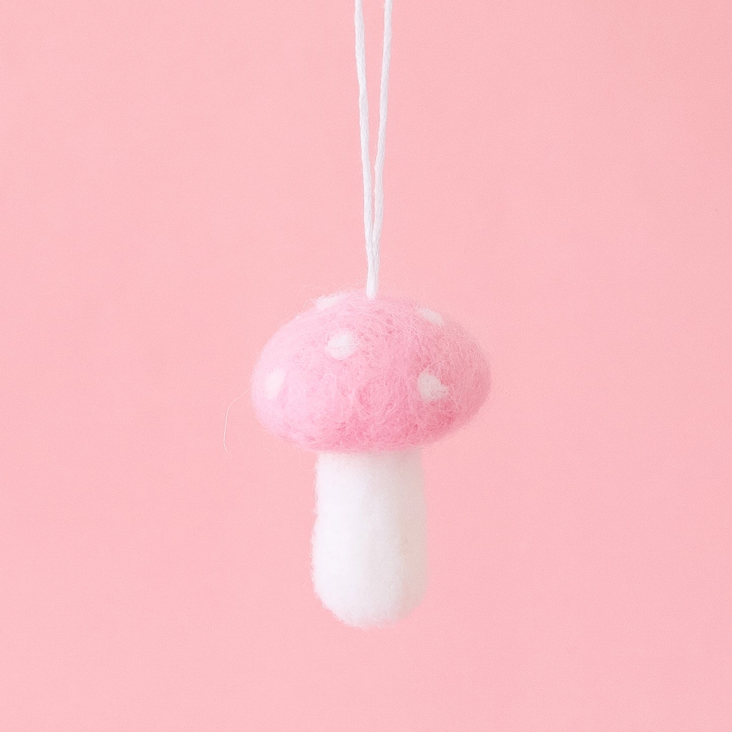 On a pink background is a felt mushroom ornament with a light pink top and cream accents.