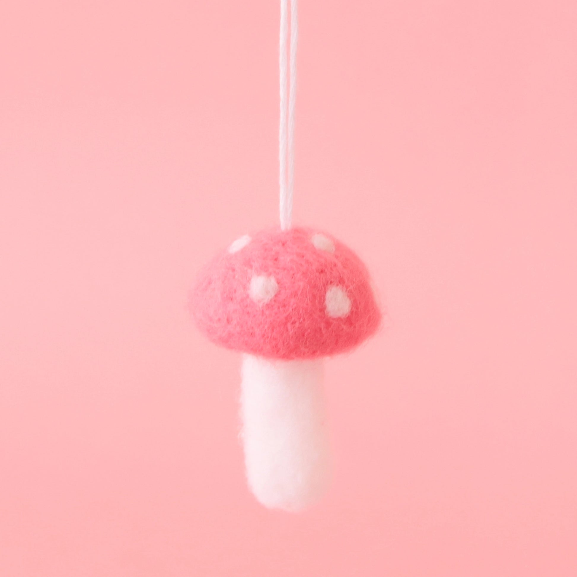 On a pink background is a felt mushroom ornament with a dark pink top and cream accents.