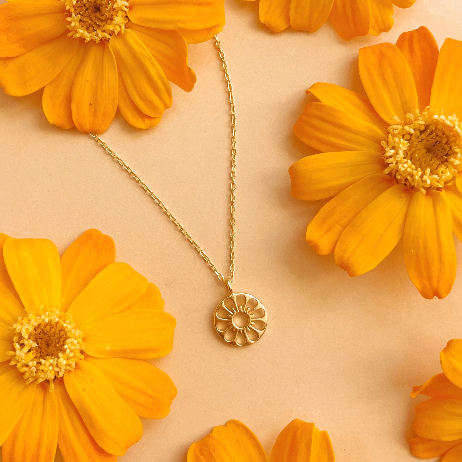 On a yellow floral background is a gold circle daisy shaped necklace. 