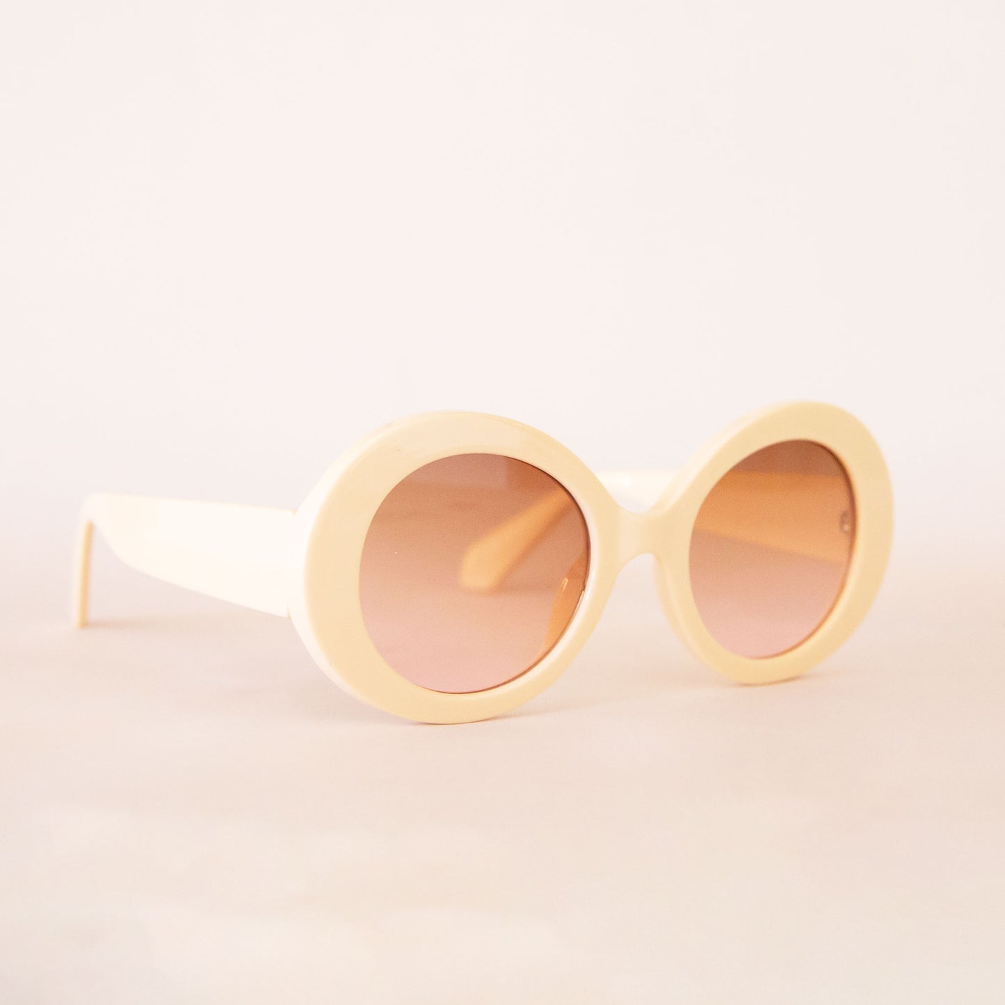 A pair of ivory round sunglasses with a cream/brown lens