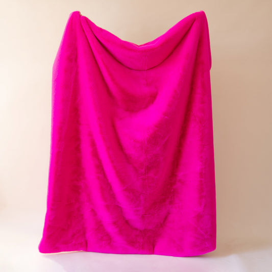 On a tan background is a bright fuchsia faux fur throw blanket.