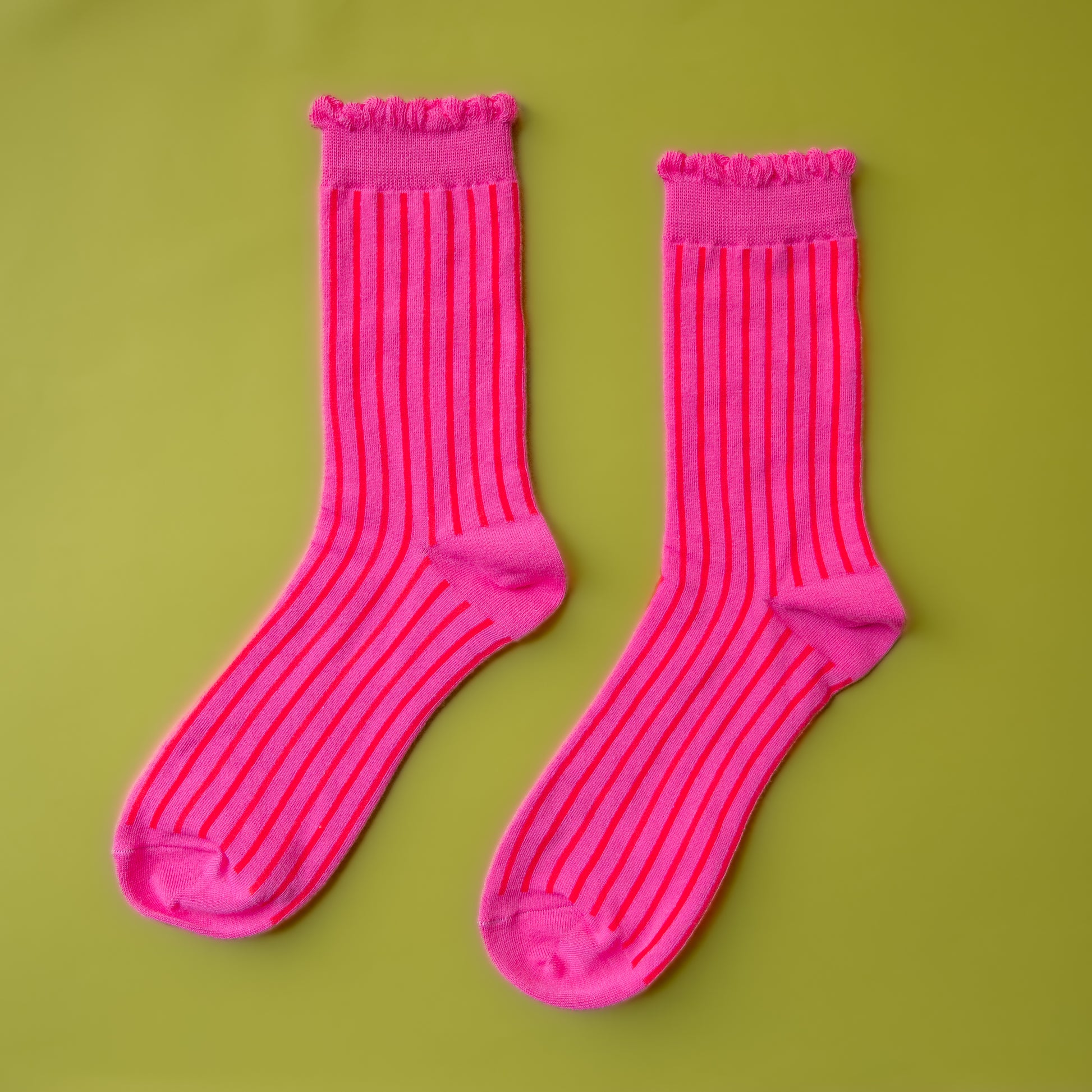 A pair of fuchsia pink crew socks with a red stripe and a ruffle edge at the top. 