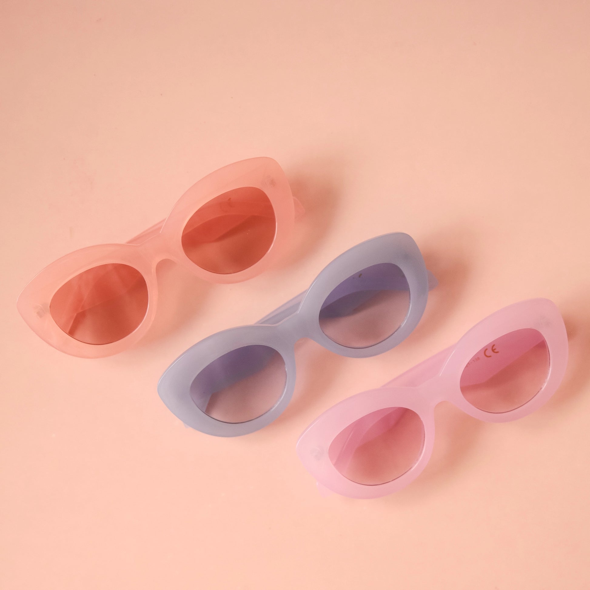 On a peachy background is a group photo of three different color options for the the Gemma Sunglass frame shape.