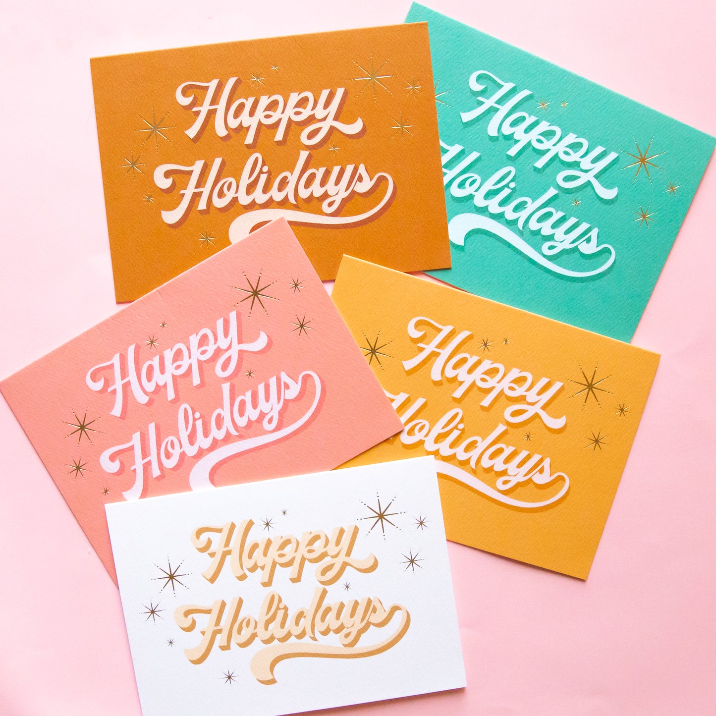 Five pack of holiday cards layered on top of each other in a parallel vertical row. The cards read 'happy Holidays' in cursive lettering. 