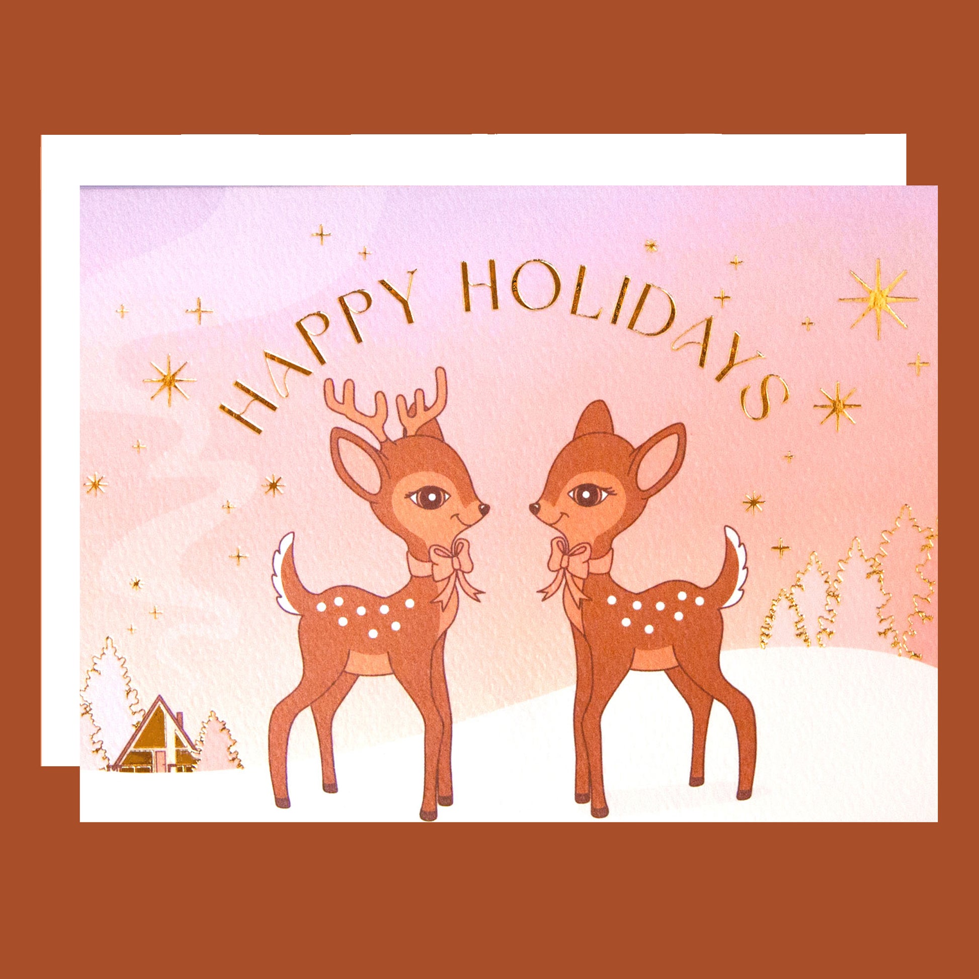 On an orange background is a greeting card with two brown retro deer graphics along with gold foiled details and text that read, "Happy Holidays".