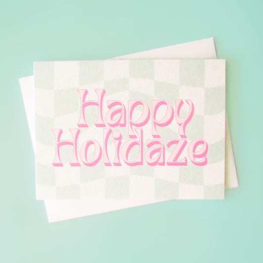 Pale mint and cream checkered card that reads 'Happy Holiday' in retro pink lettering with thin magenta shadow. The card is accompanied by a solid white envelope.