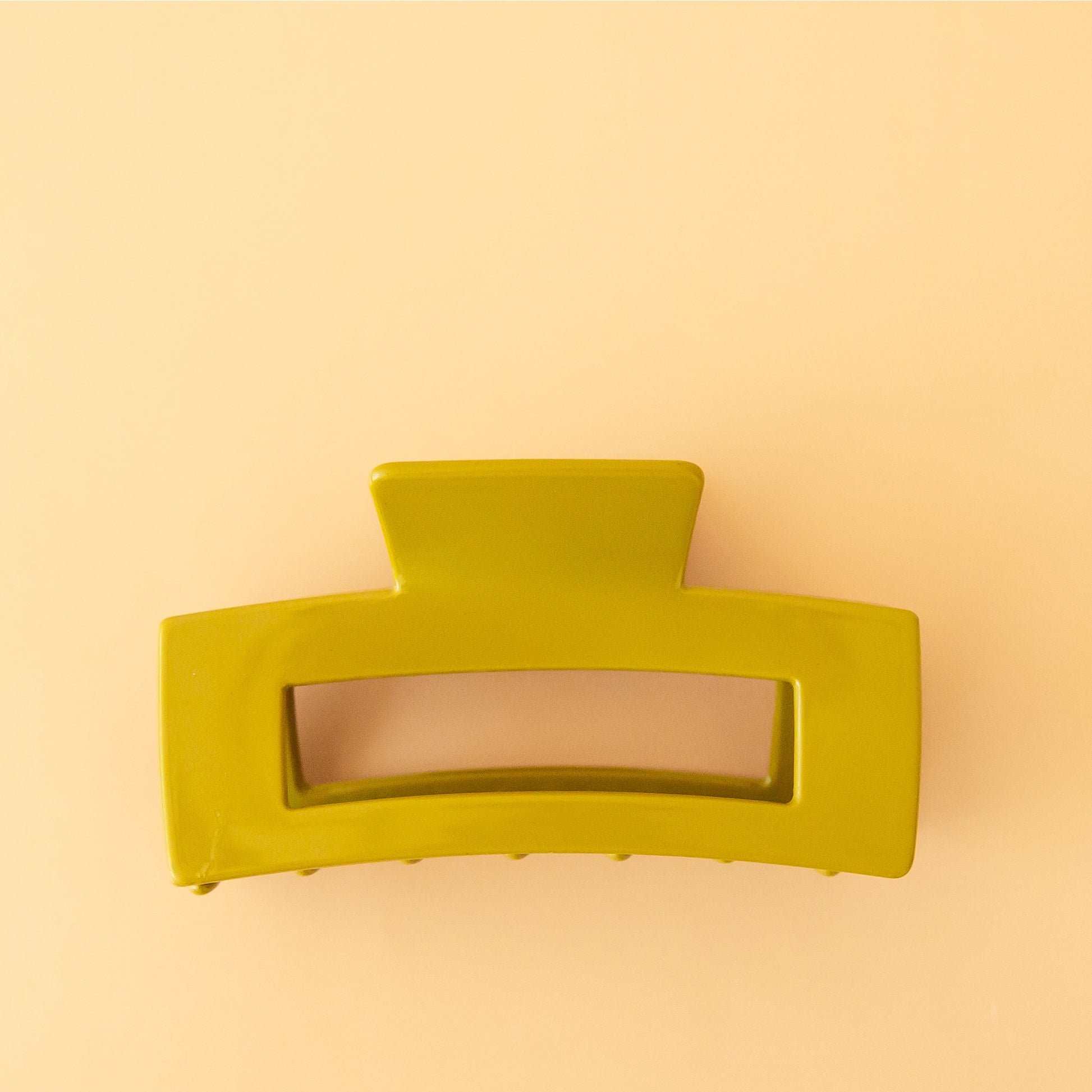 On a peachy background is the rectangular claw clip in the shade avocado which features a vibrant green shade. 