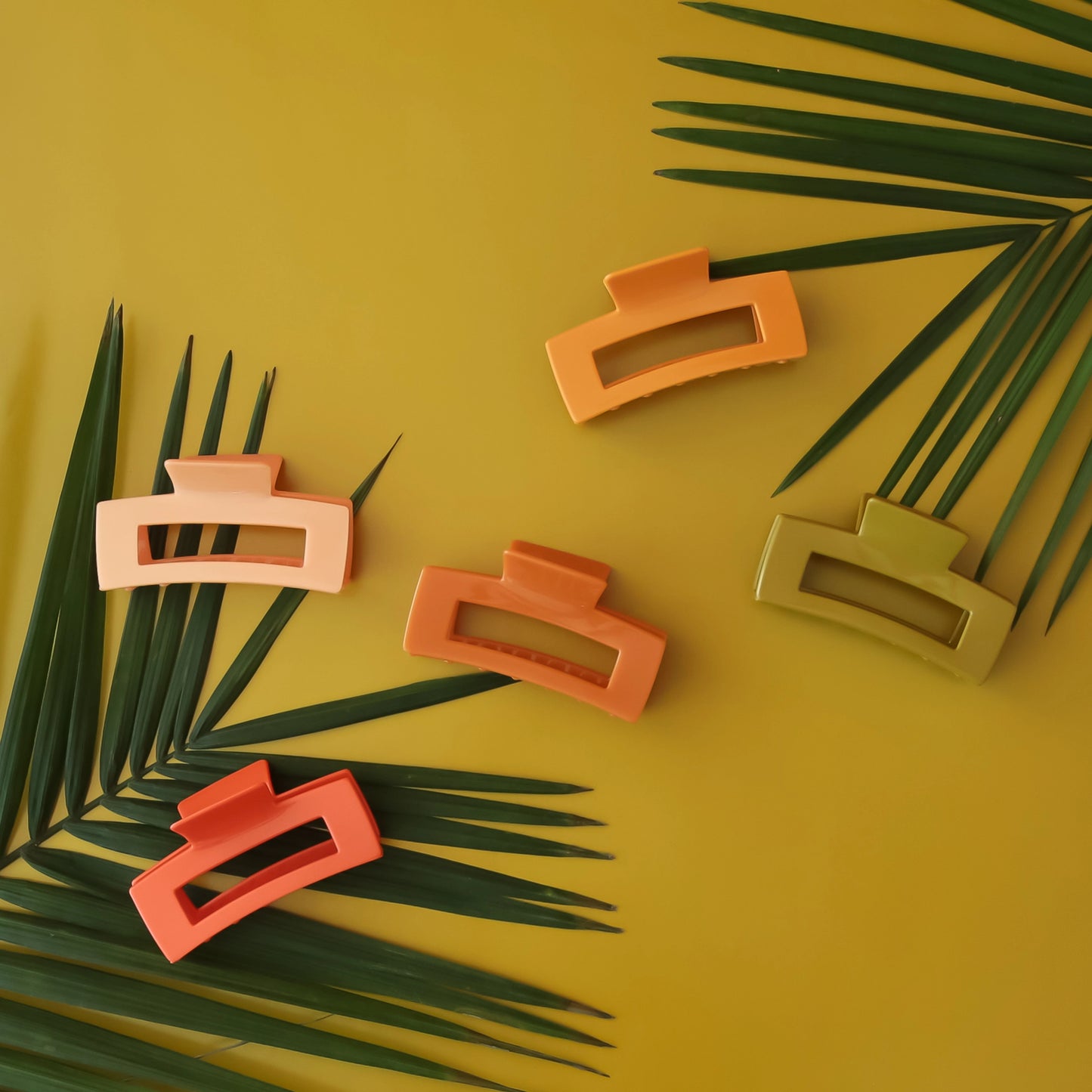 On a green background is a variety of rectangle claw clips in different colors on a green palm leaf.