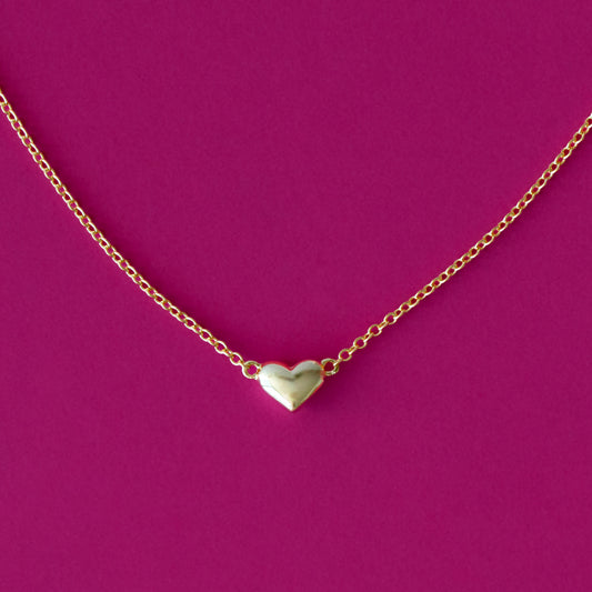 A bubble shaped gold heart necklace on a hot pink background.