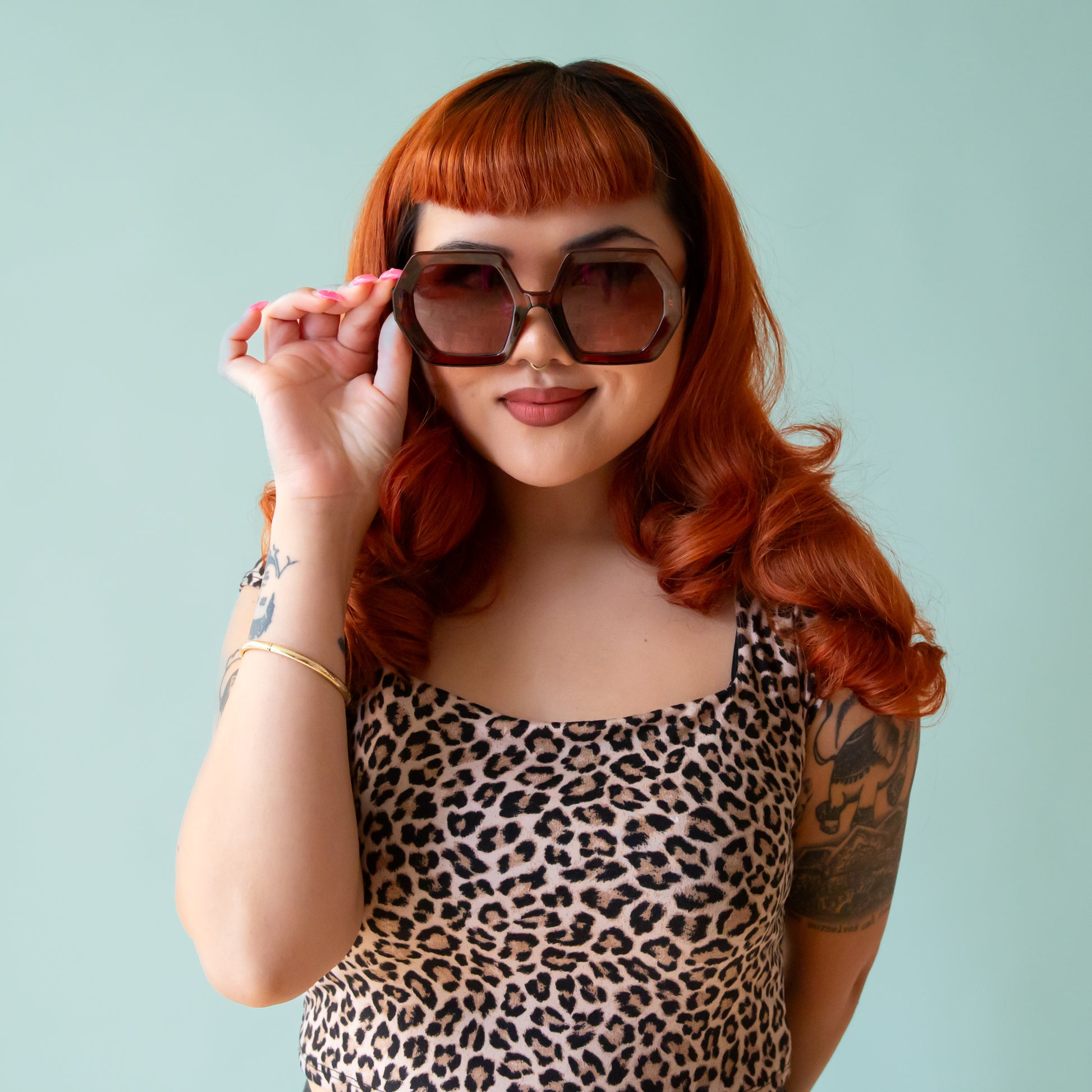 On a peachy background is a pair of hexagon shaped sunglasses in a cognac brown color.
