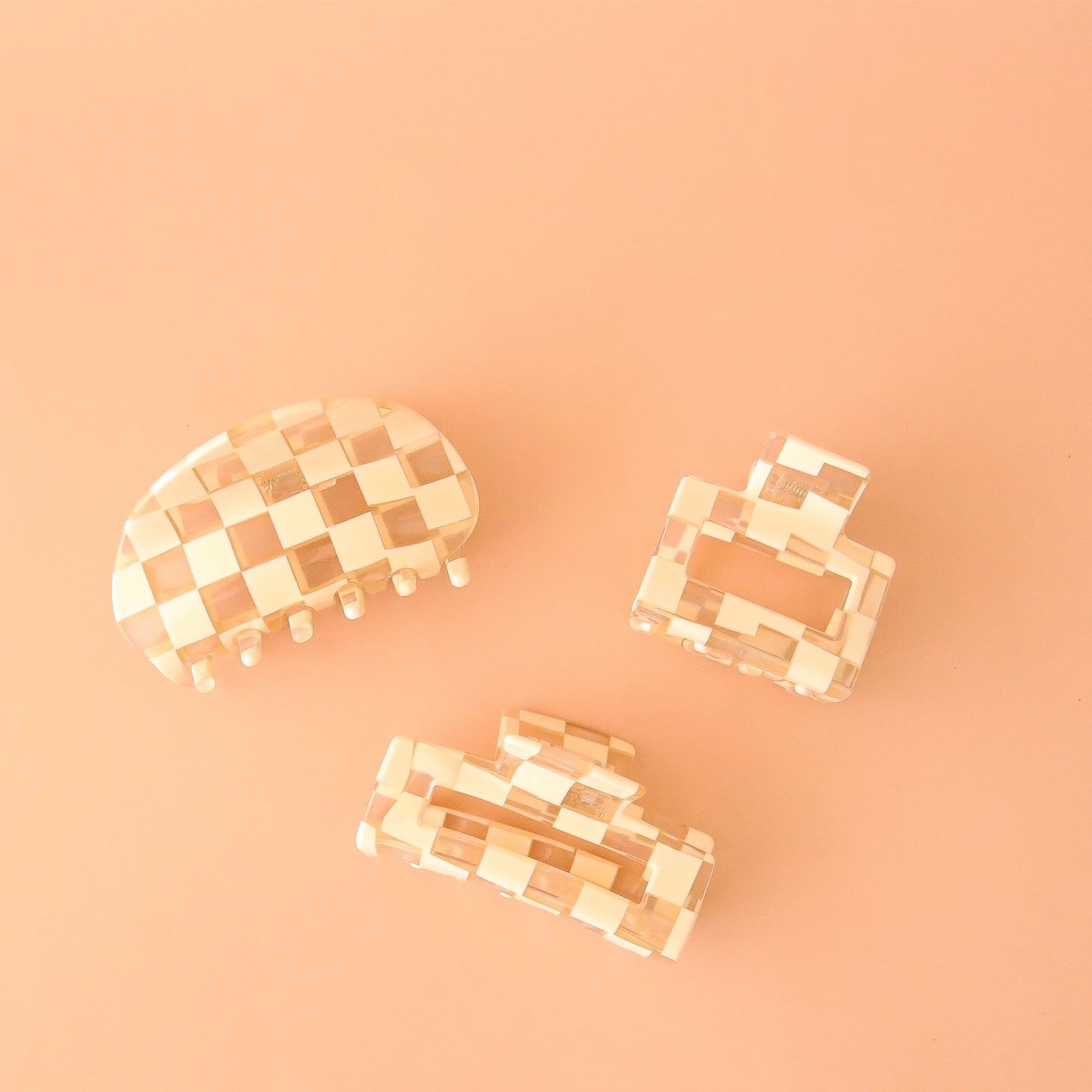 On a peachy background is three different shaped white claw clips. One with a rounded edge, one smaller square shape and one large rectangular shape. 