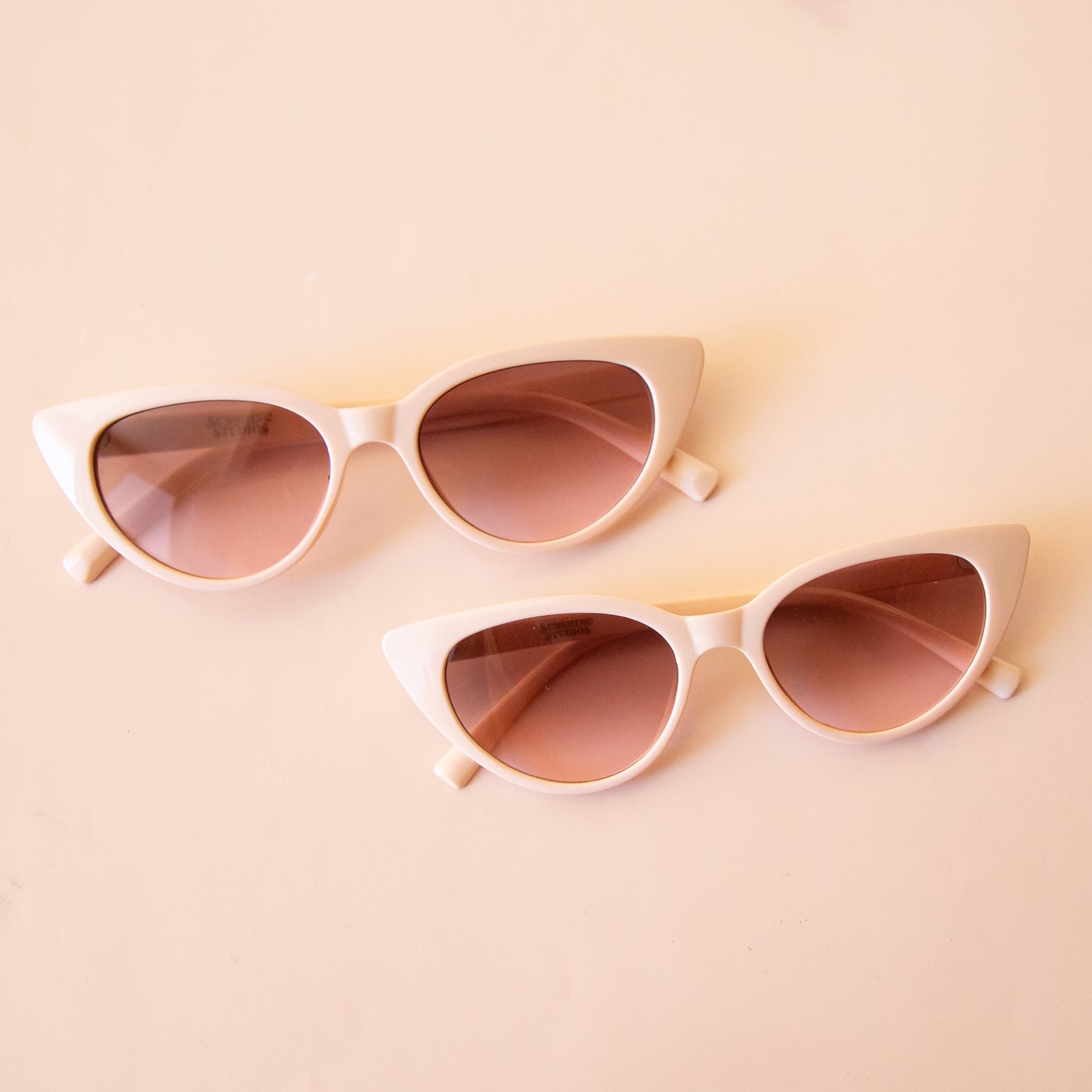 An ivory pair of cat-eye shaped sunglasses with a brown lens. 