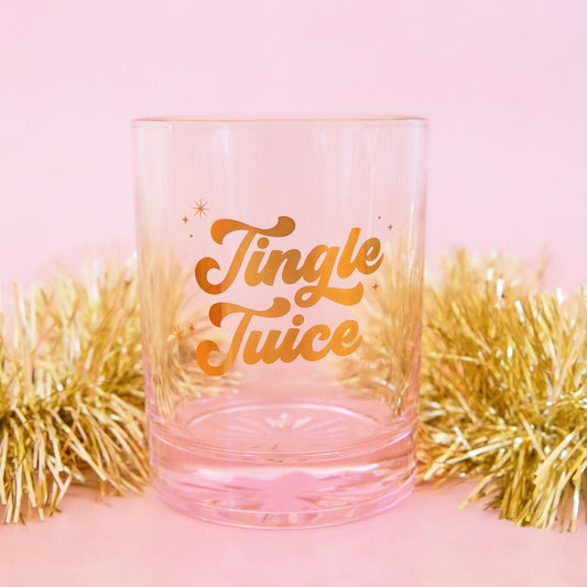 Glass cup with gold lettering is shown against a pink background