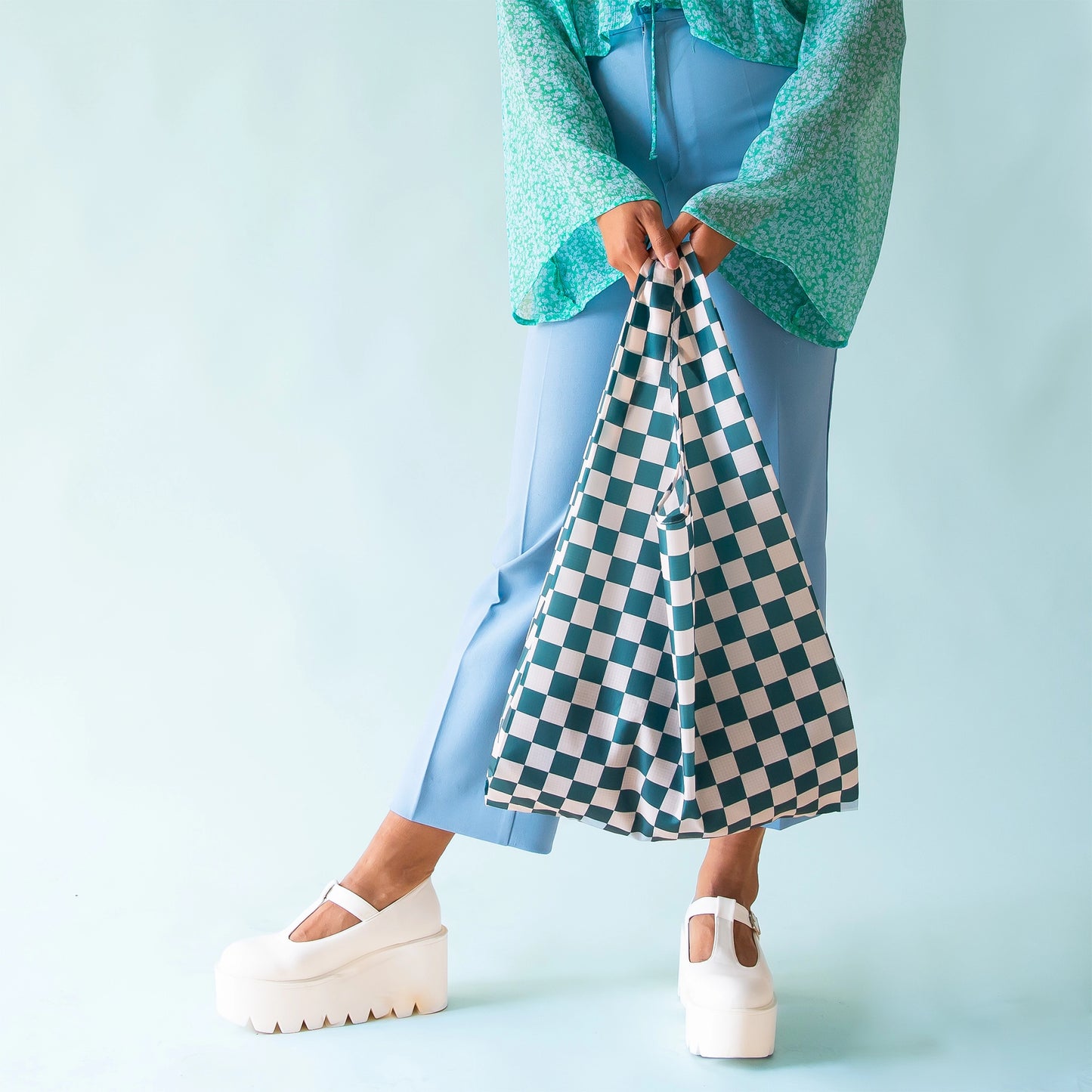 On a light blue background is a dark teal checkered nylon tote bag.