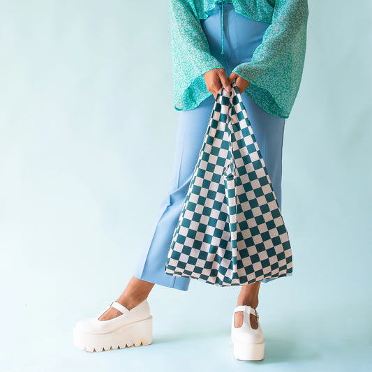 On a light blue background is a dark teal checkered nylon tote bag.
