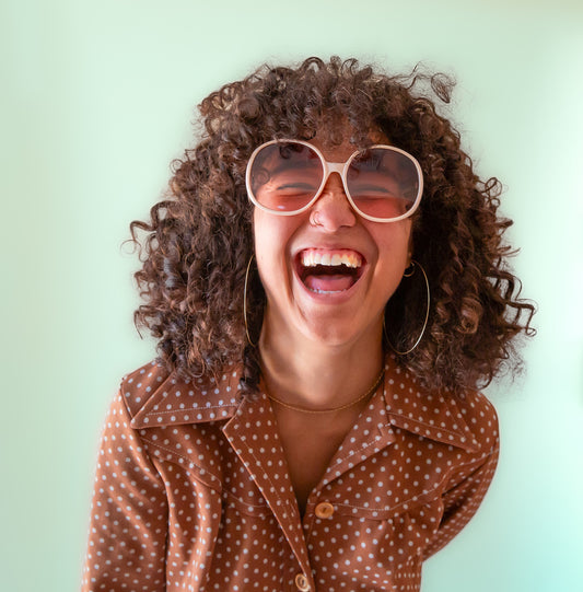 A creamy white pair of round oversized sunglasses with a light brown / pink lens.