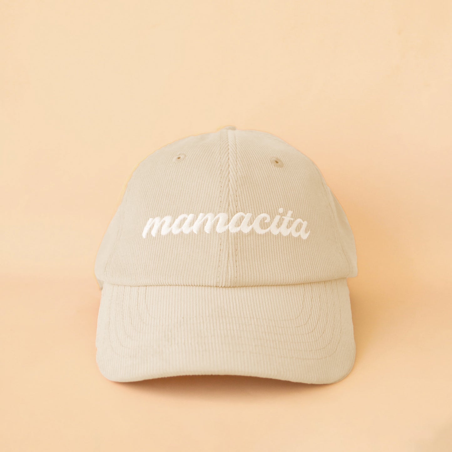Oat colored baseball hat, with corduroy materials. On the front of the hat in white stitching it says "mamacita". 