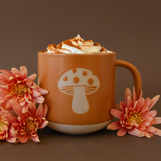 On a pink background is a ceramic mug with a light colored mushroom design.