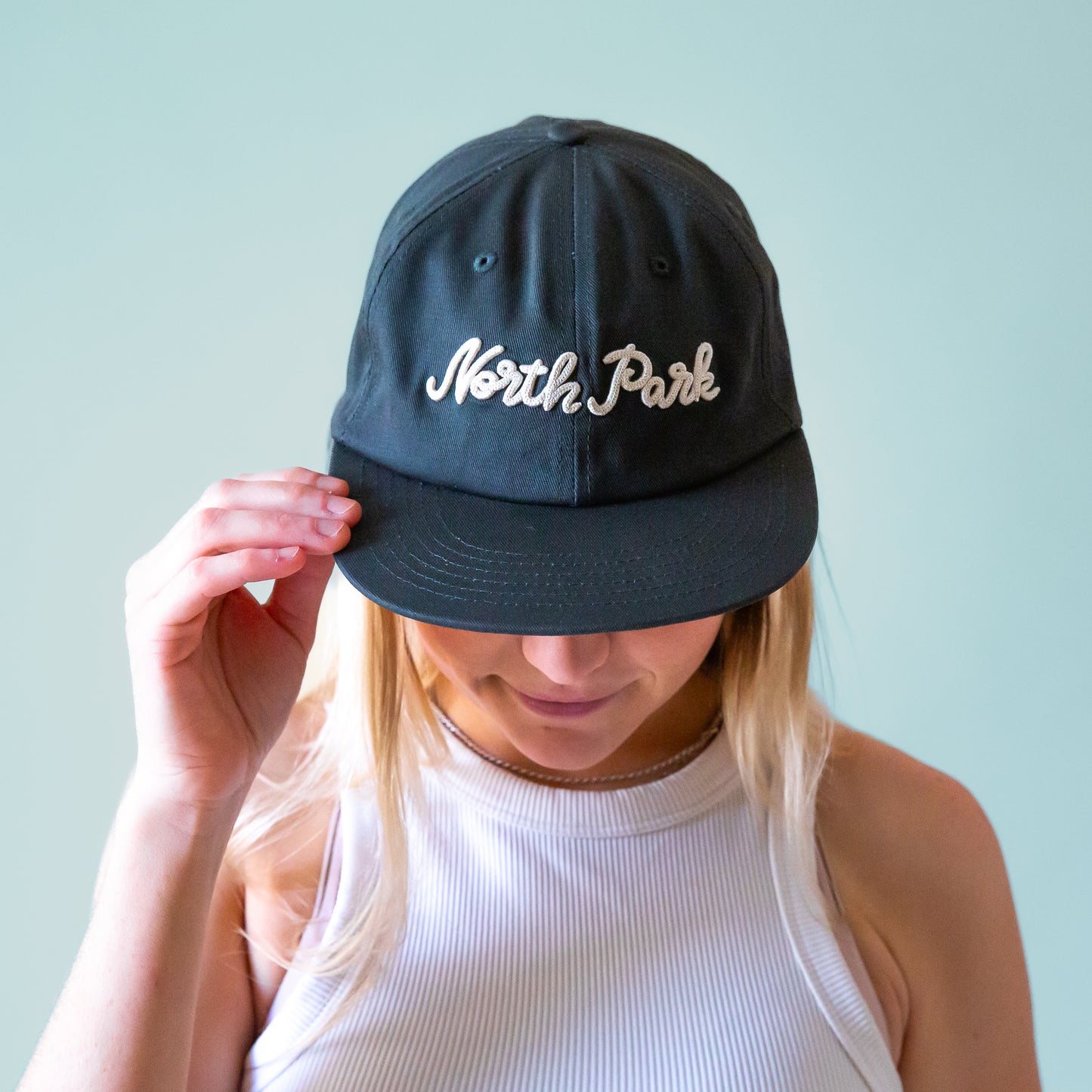 A dark greenish blue flat brim hat with white embroidered text that reads, 'North Park'. 