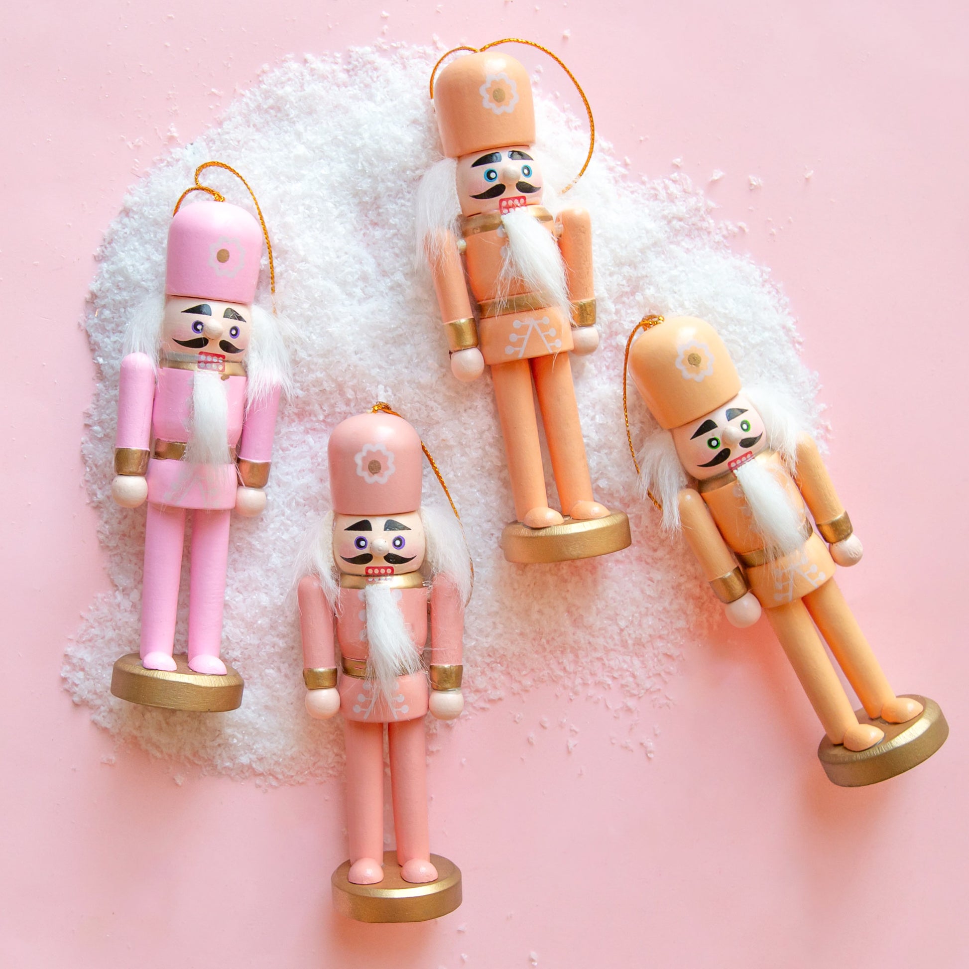 A set of four nutcracker ornaments in a variation of orange and pink tones with flowers on their hats. 