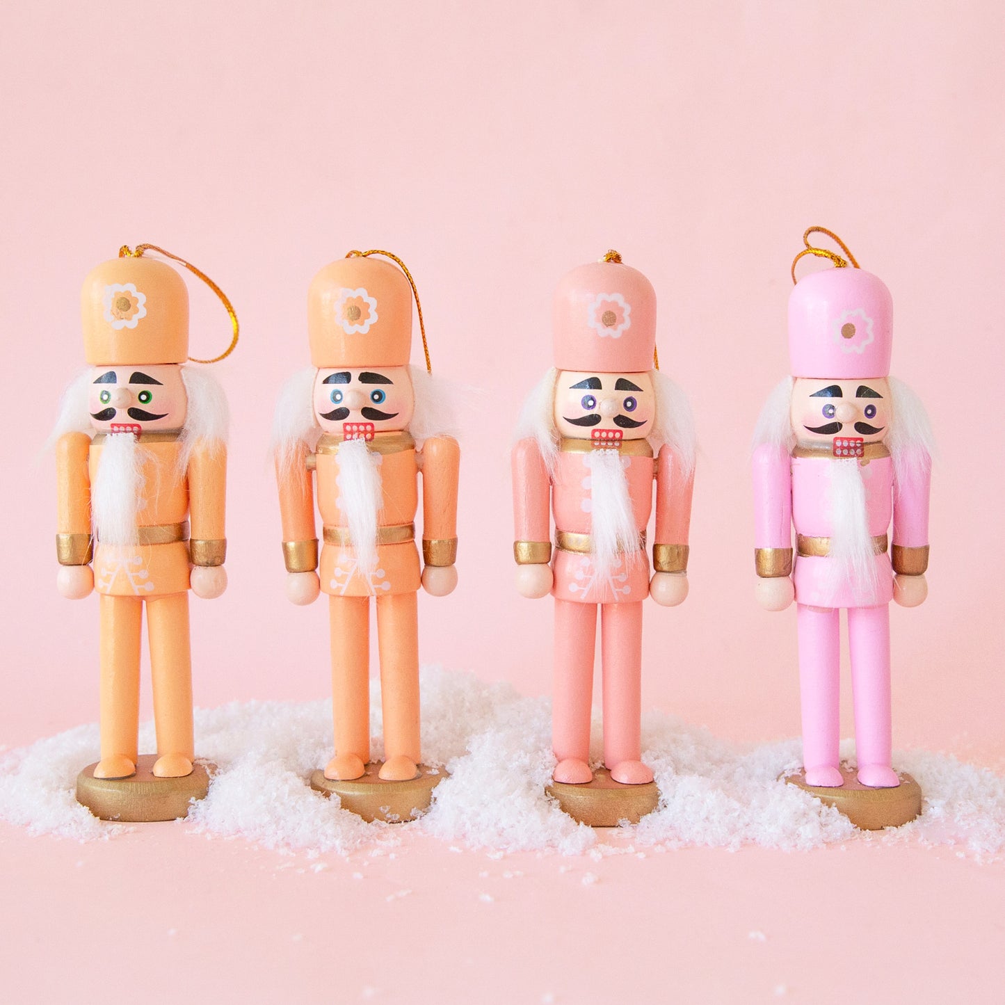 A set of four nutcracker ornaments in a variation of orange and pink tones with flowers on their hats. 