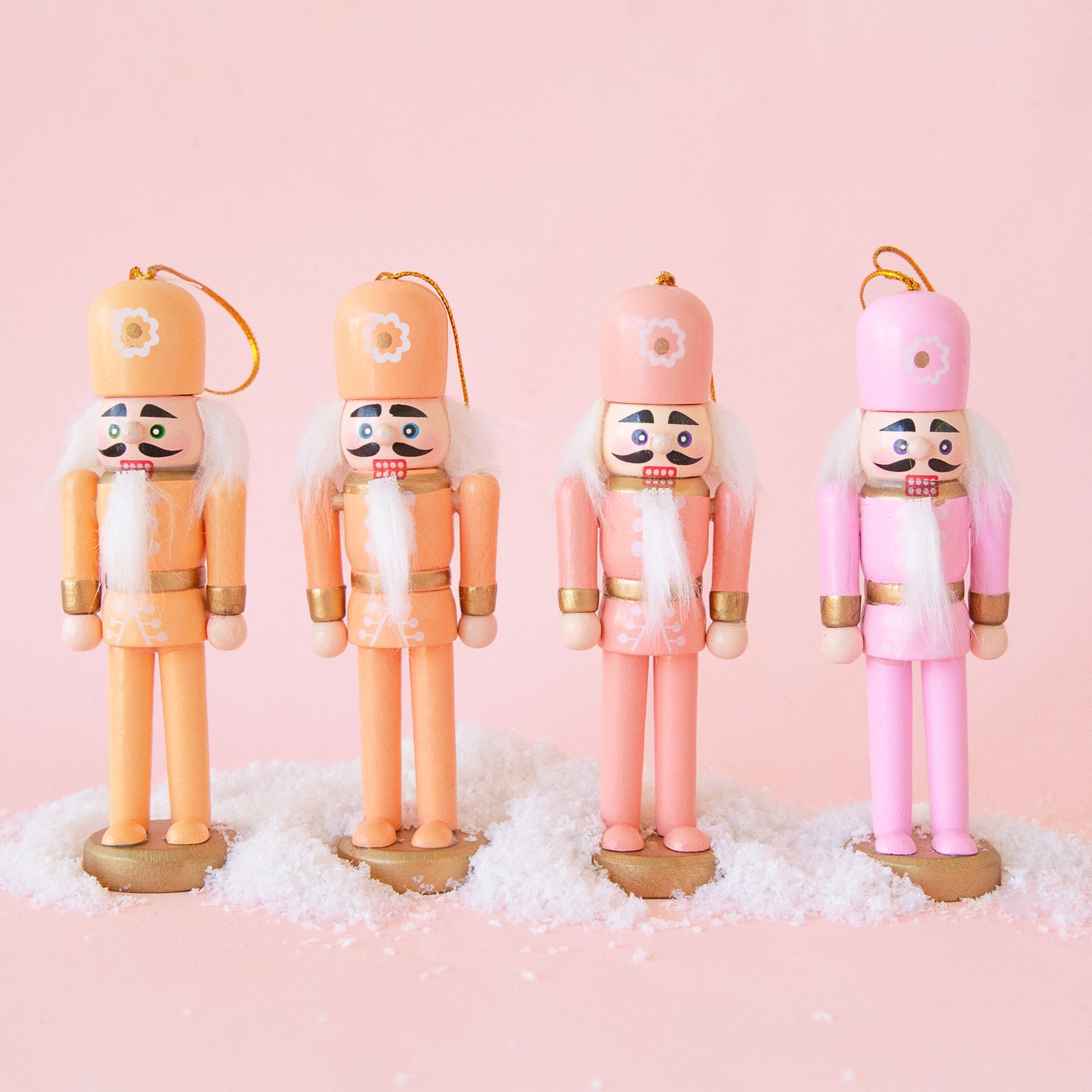 A set of four nutcracker ornaments in a variation of orange and pink tones with flowers on their hats. 