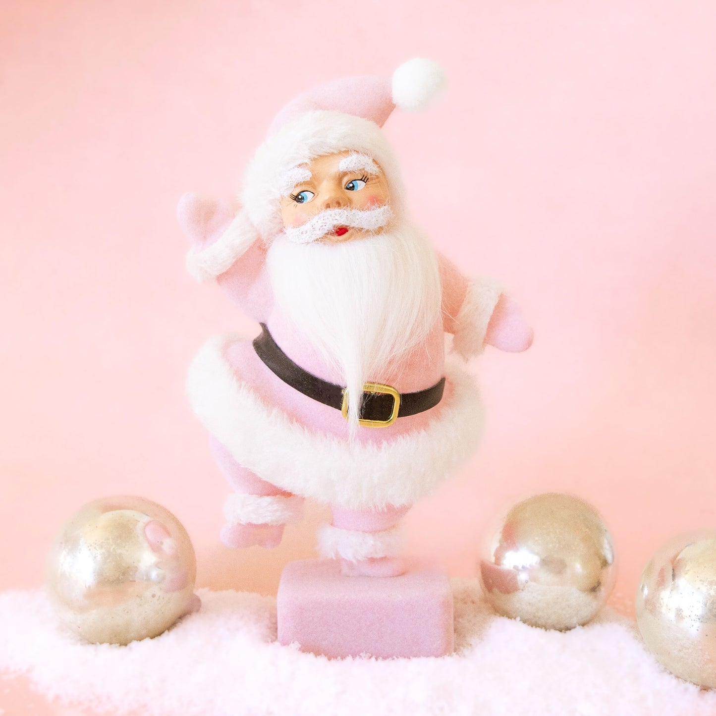On a pink background is a Santa figurine with a pink flocked suit and white furry details. 