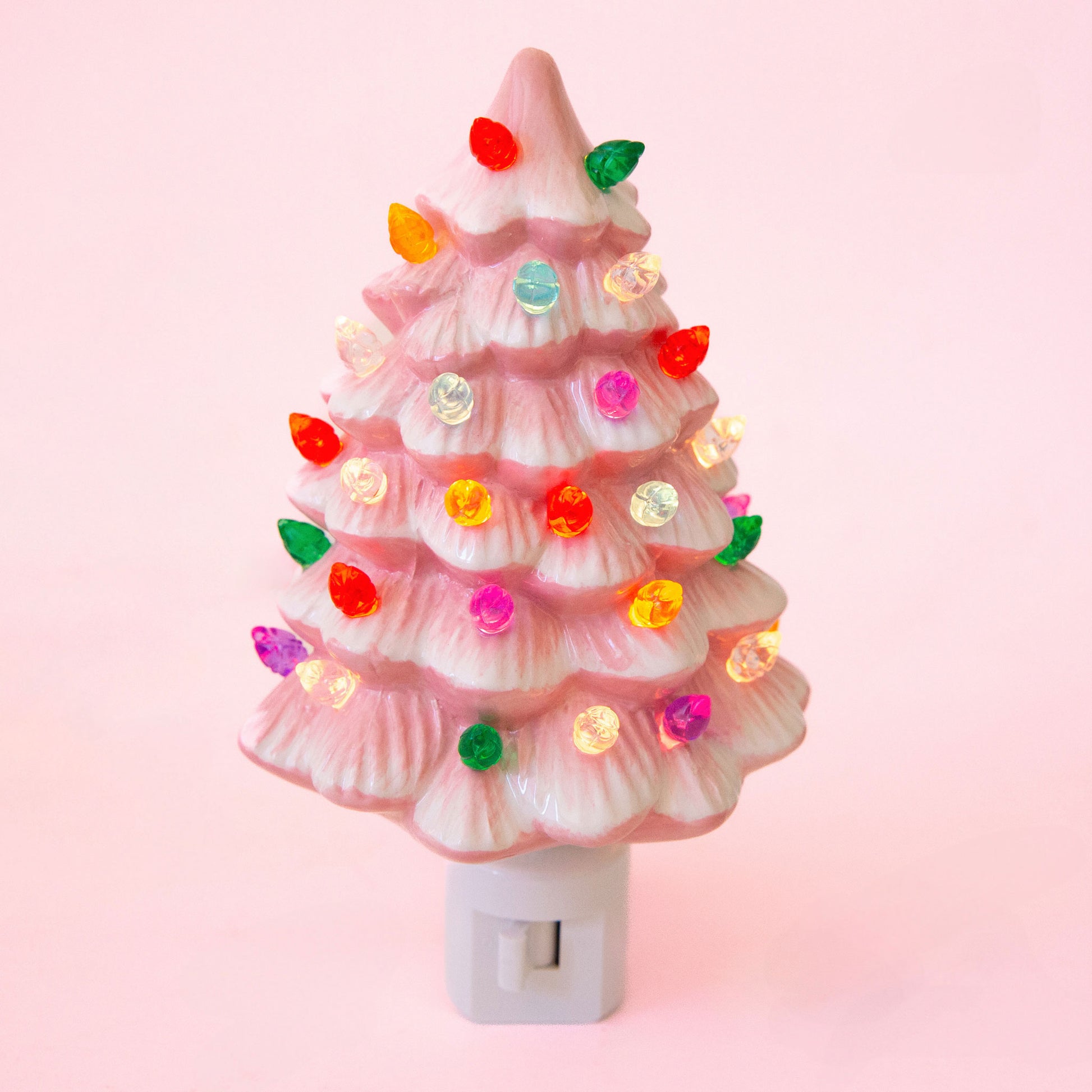 A ceramic christmas tree shaped night light.  The night light has multi colored lights all over it and the ceramic is pink.