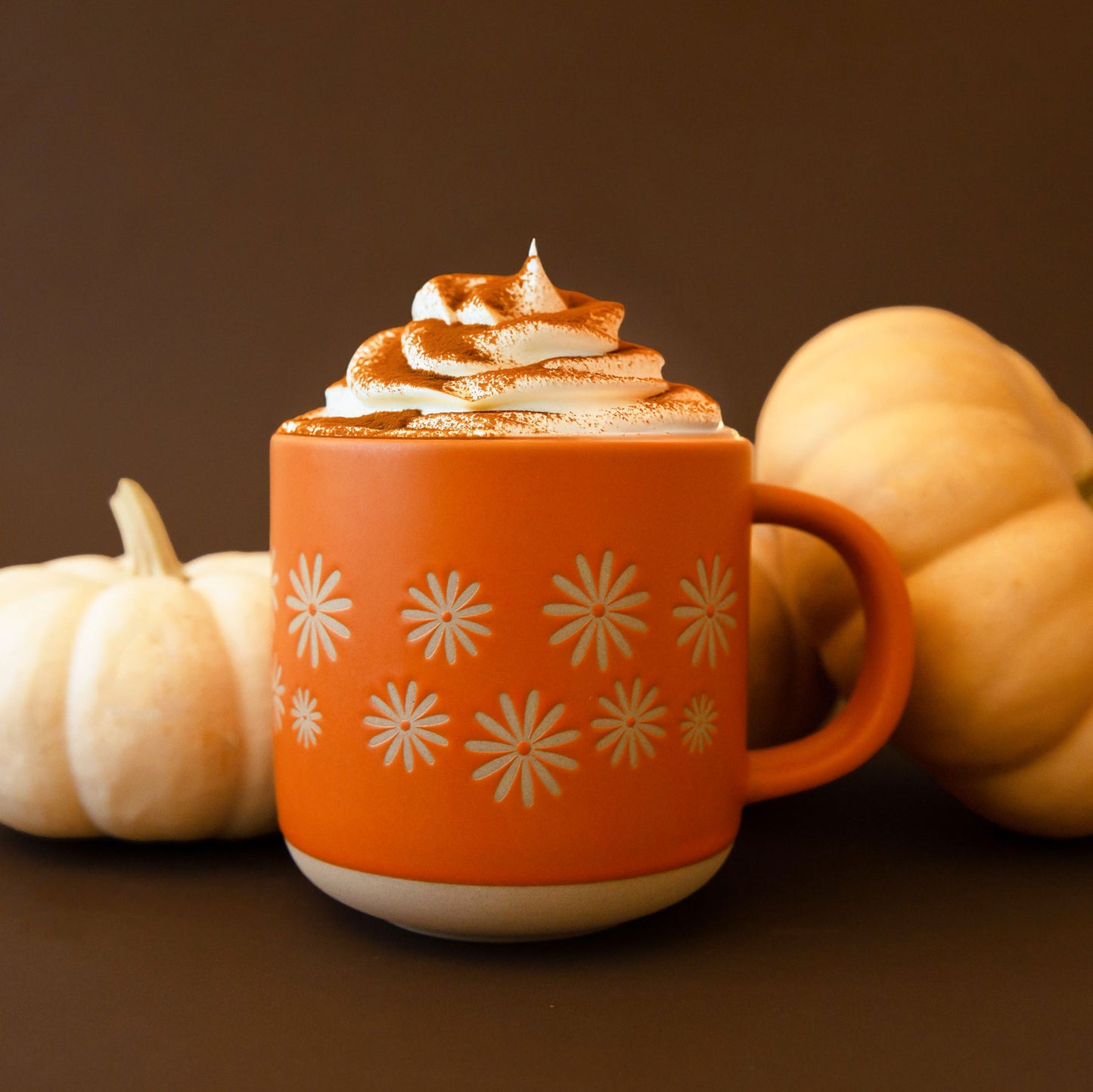 A ceramic orange mug with small pinwheel daisy flower shapes around the center.
