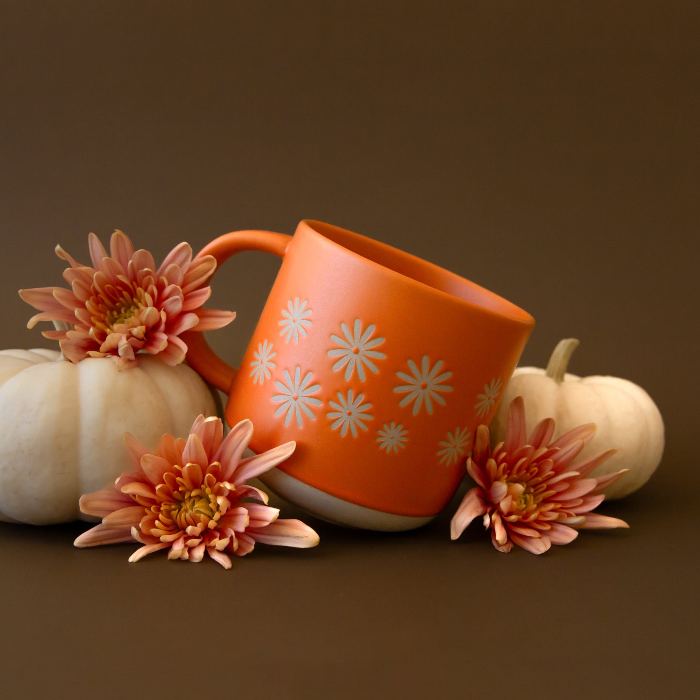 A ceramic orange mug with small pinwheel daisy flower shapes around the center.