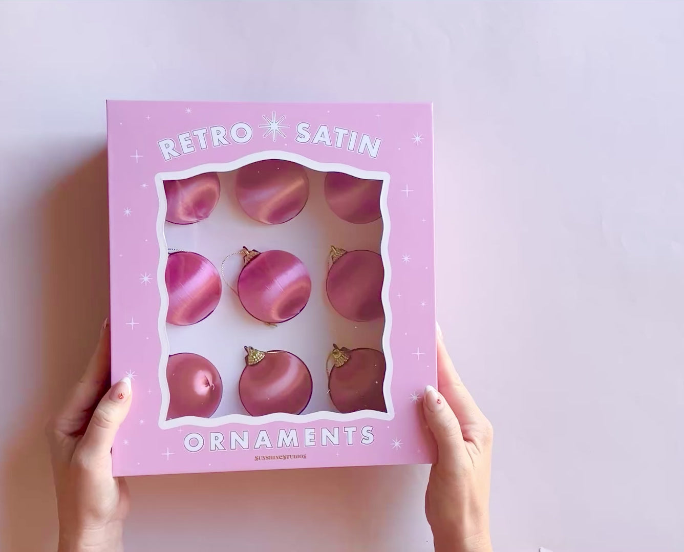 Hands opening a pink box that reads "retro satin ornaments".  Inside the box are 9 round pink and orange hue satin ball ornaments.