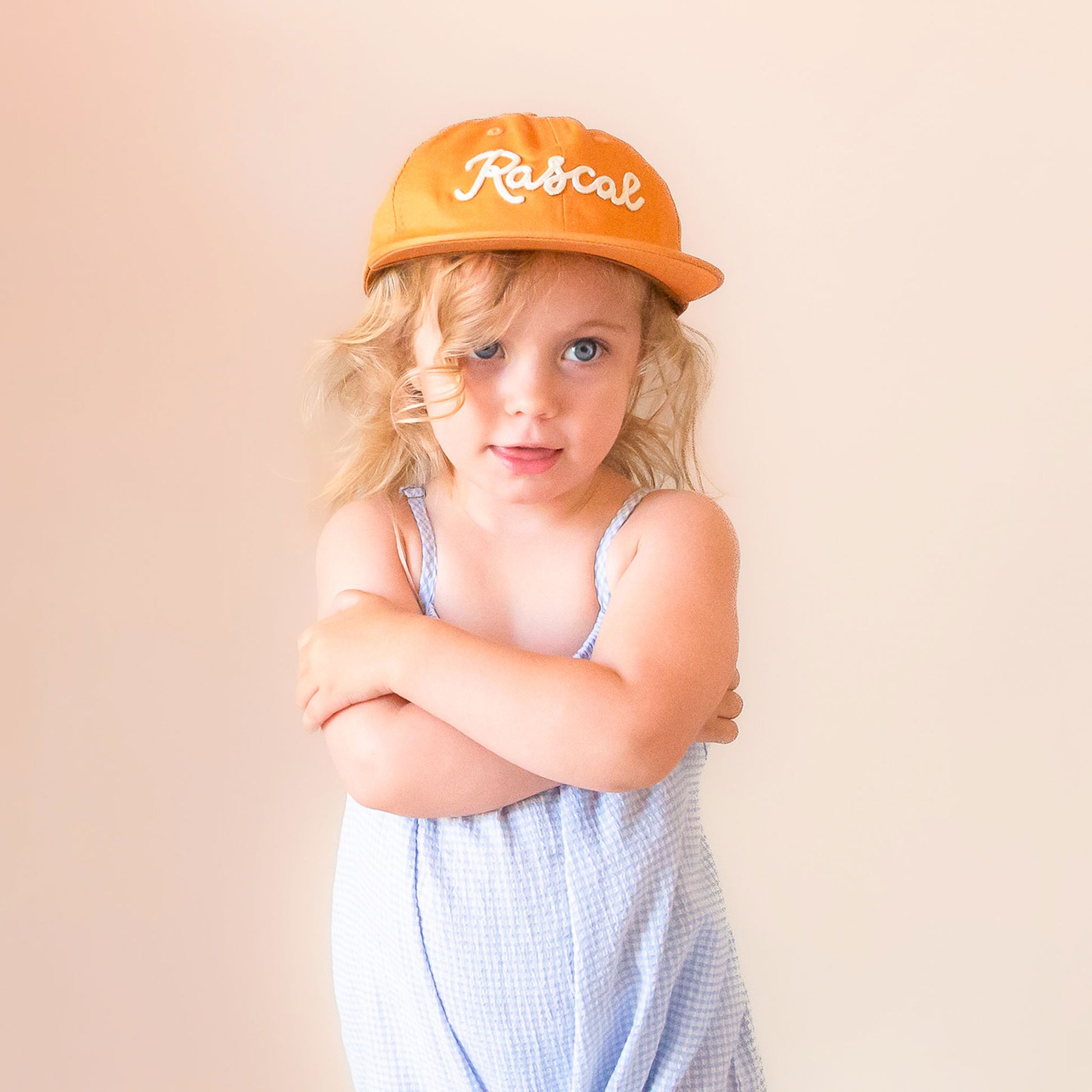 A burnt orange flat brimmed hat with white embroidered text that reads, "Rascal".