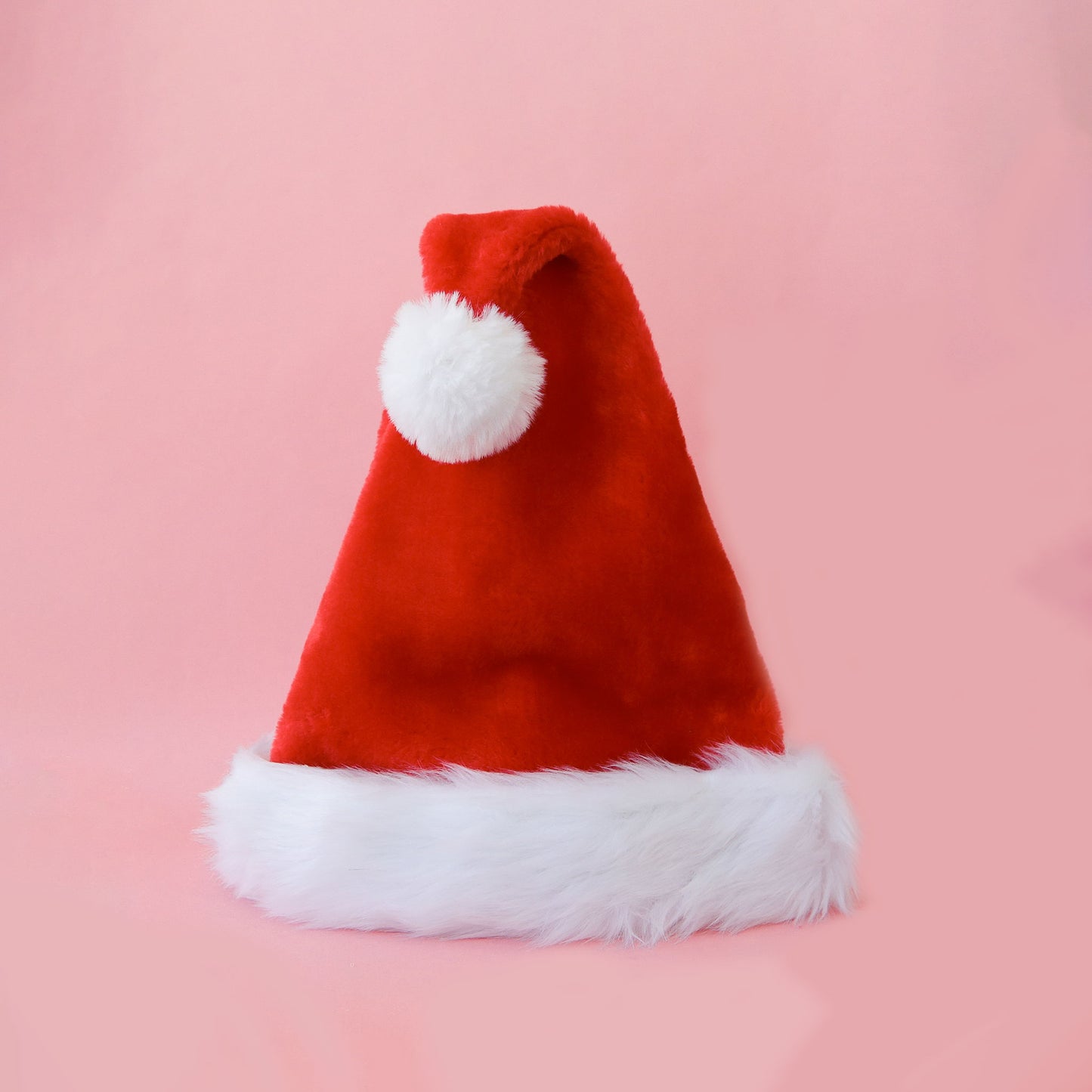 On a pink background is a red Santa hat with white accents and faux fur. 