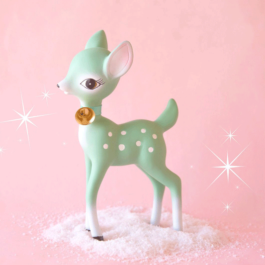 On a peachy background is a brown retro deer figurine with white spots and details, a sweet expression and a gold bell on the front of their neck.