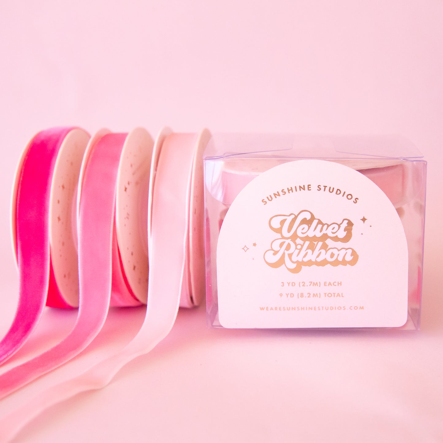 On a pink background is a pack of three pink velvet ribbon spools. 