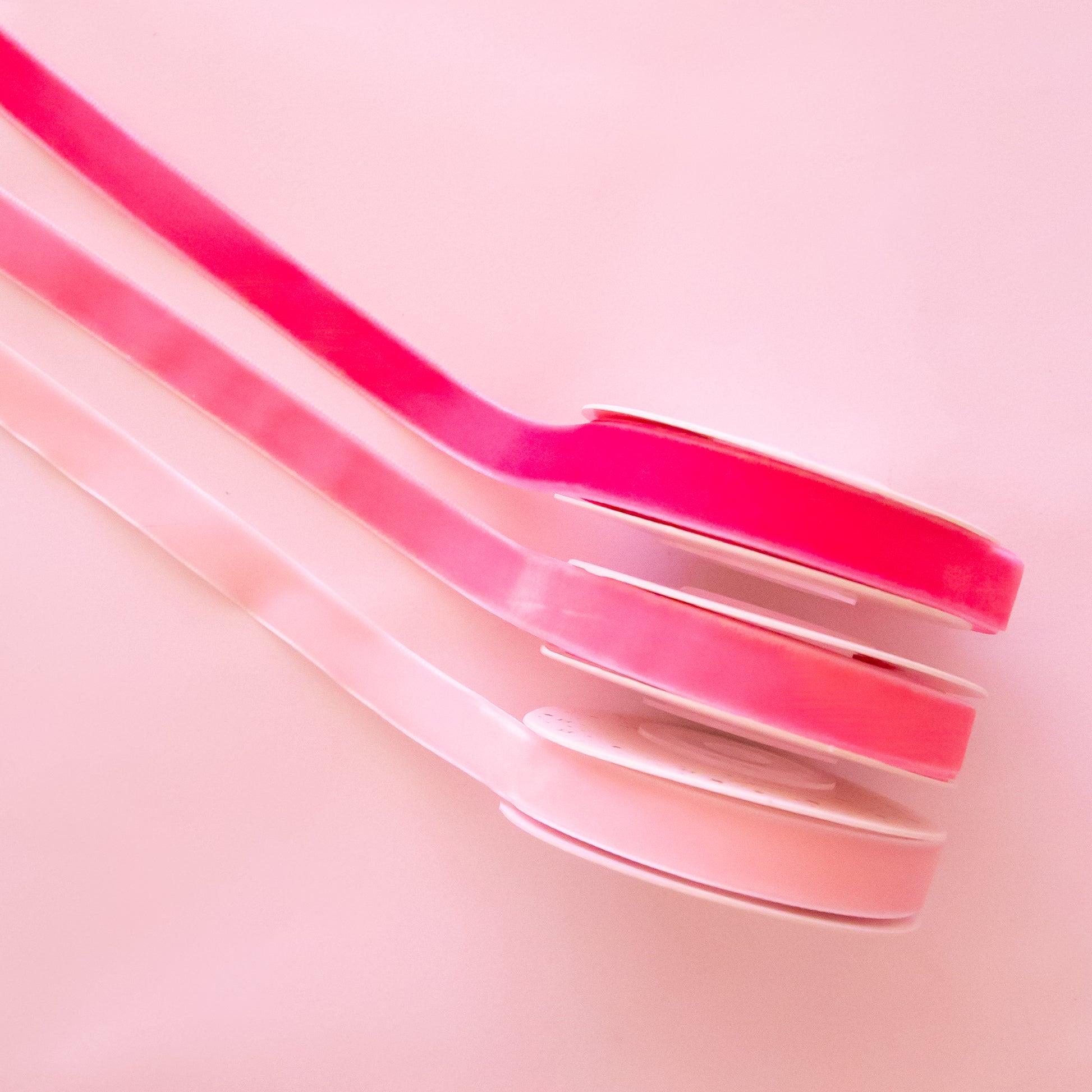 On a pink background is a pack of three pink velvet ribbon spools. 