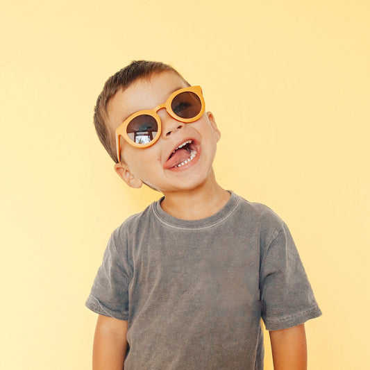 On a light yellow background is. children's model wearing a pair of round sunglasses in a yellow shade. 