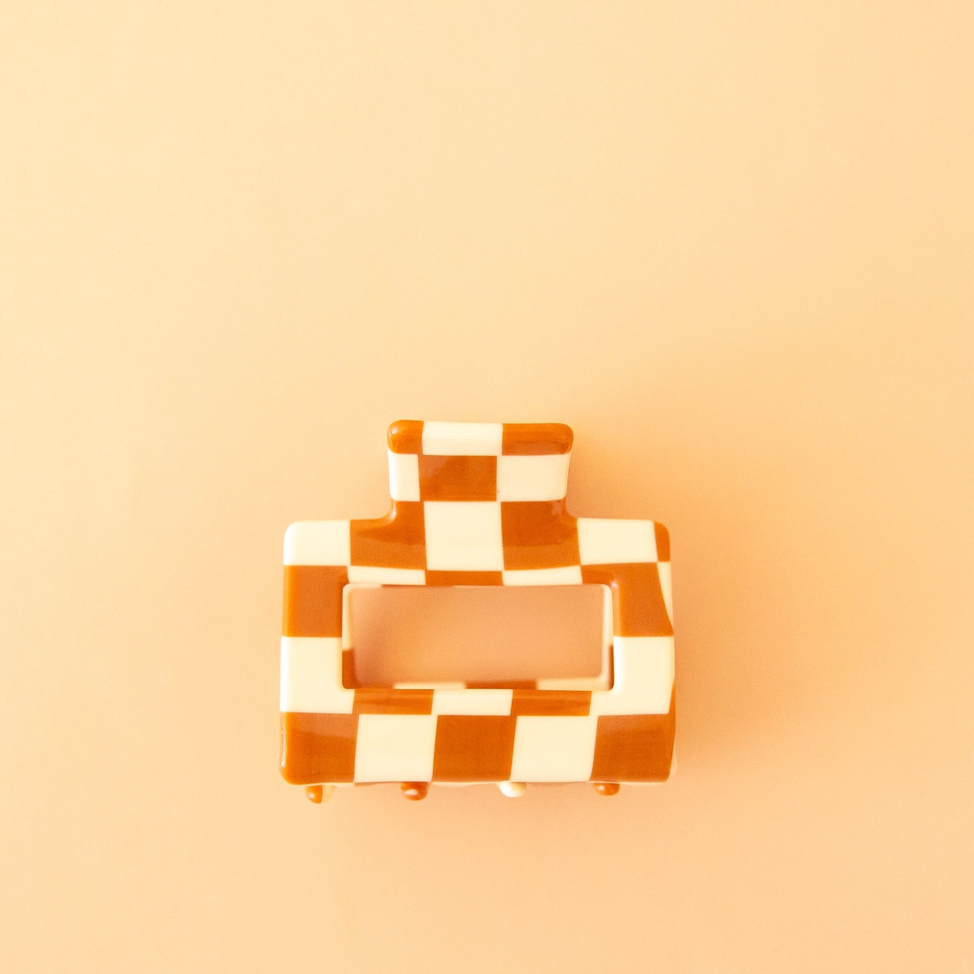 On a tan background is an ivory and orange square claw clip.