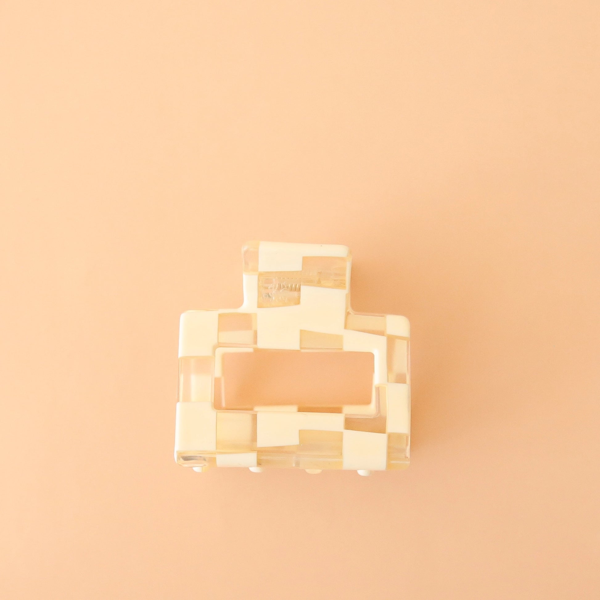 On a peachy background is a square ivory and clear claw clip. 