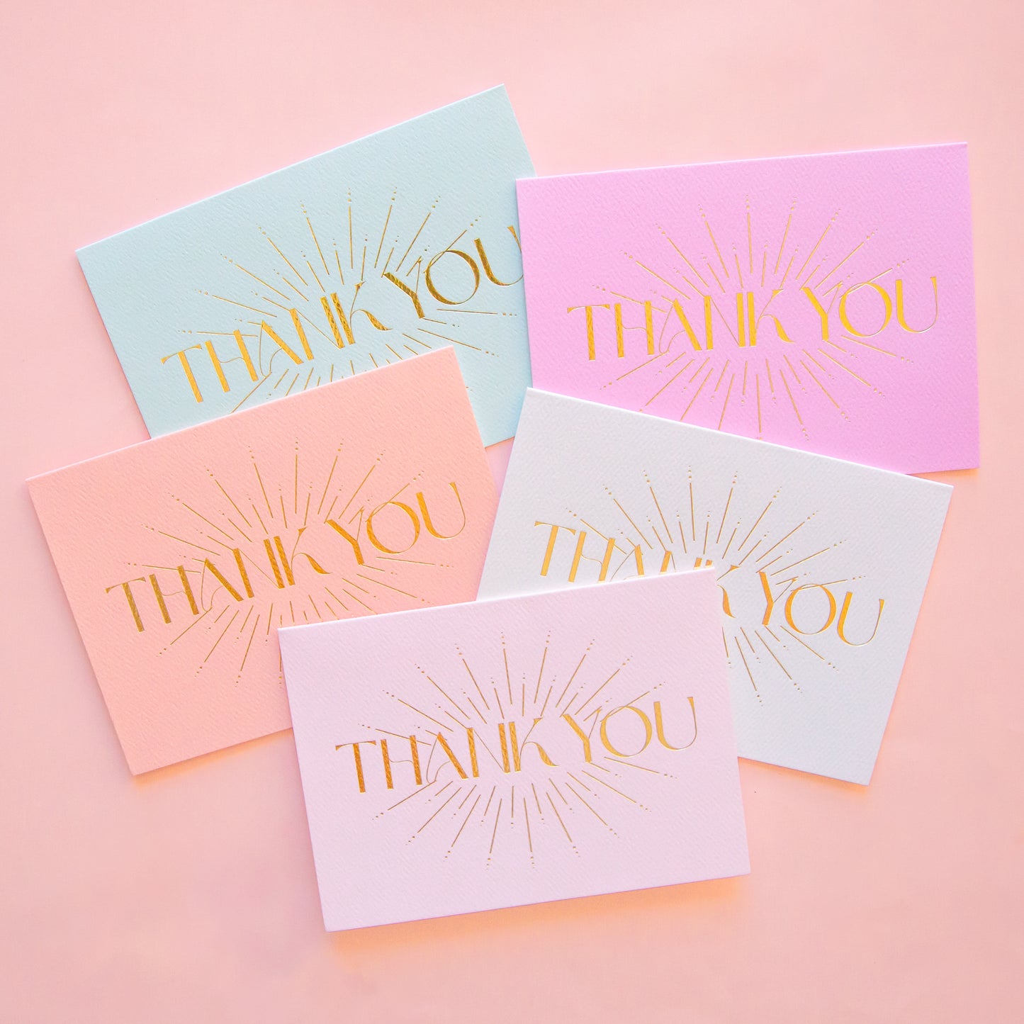 On an ivory background is five different colored thank you cards with gold foiled letters in the center that read, "Thank You". The colors come in fuchsia, mint green, light pink, white and salmon. 