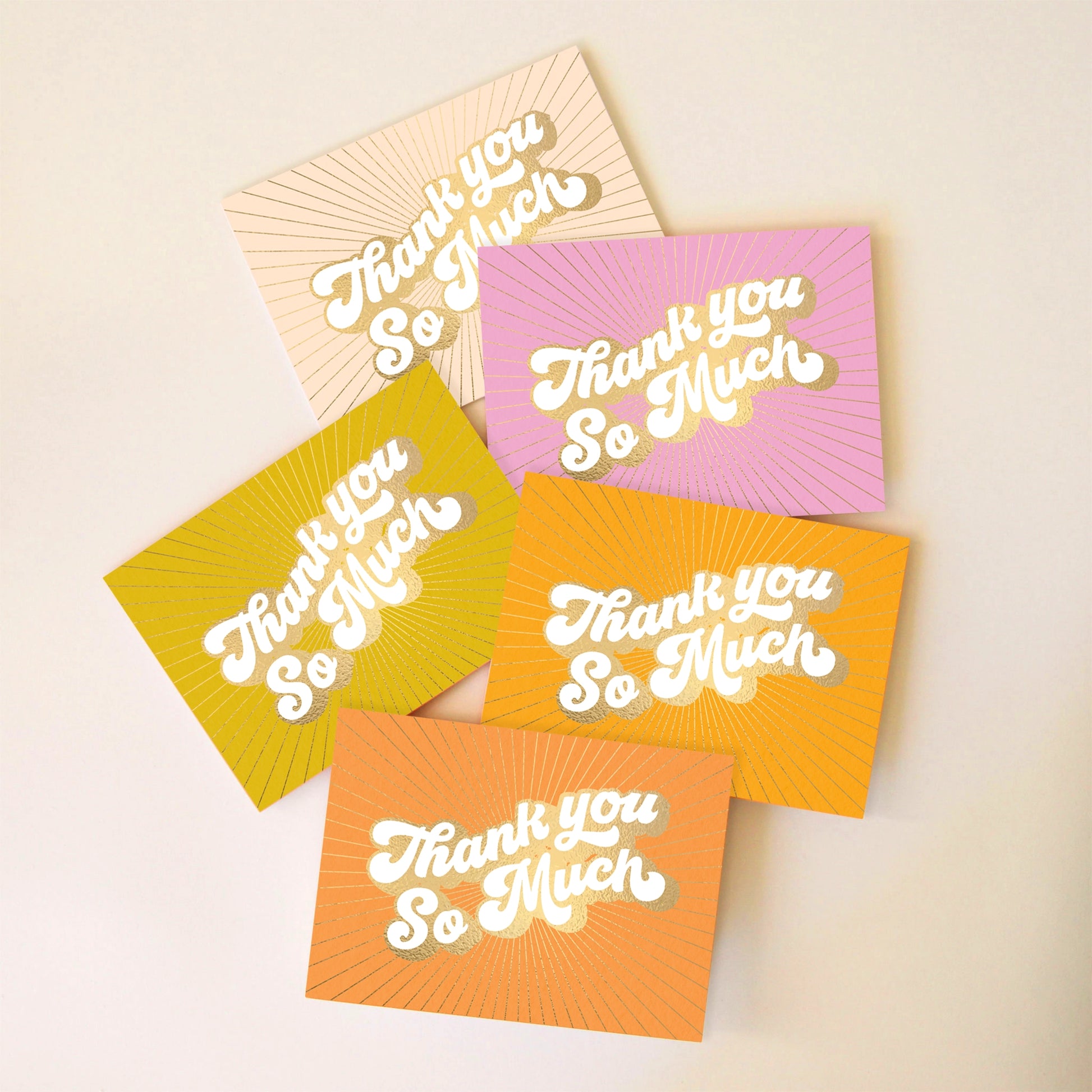 On an ivory background is a pack of 5 thank you cards in a variety of colors that all read, "Thank You So Much" in white letters and gold foiled outlined. 